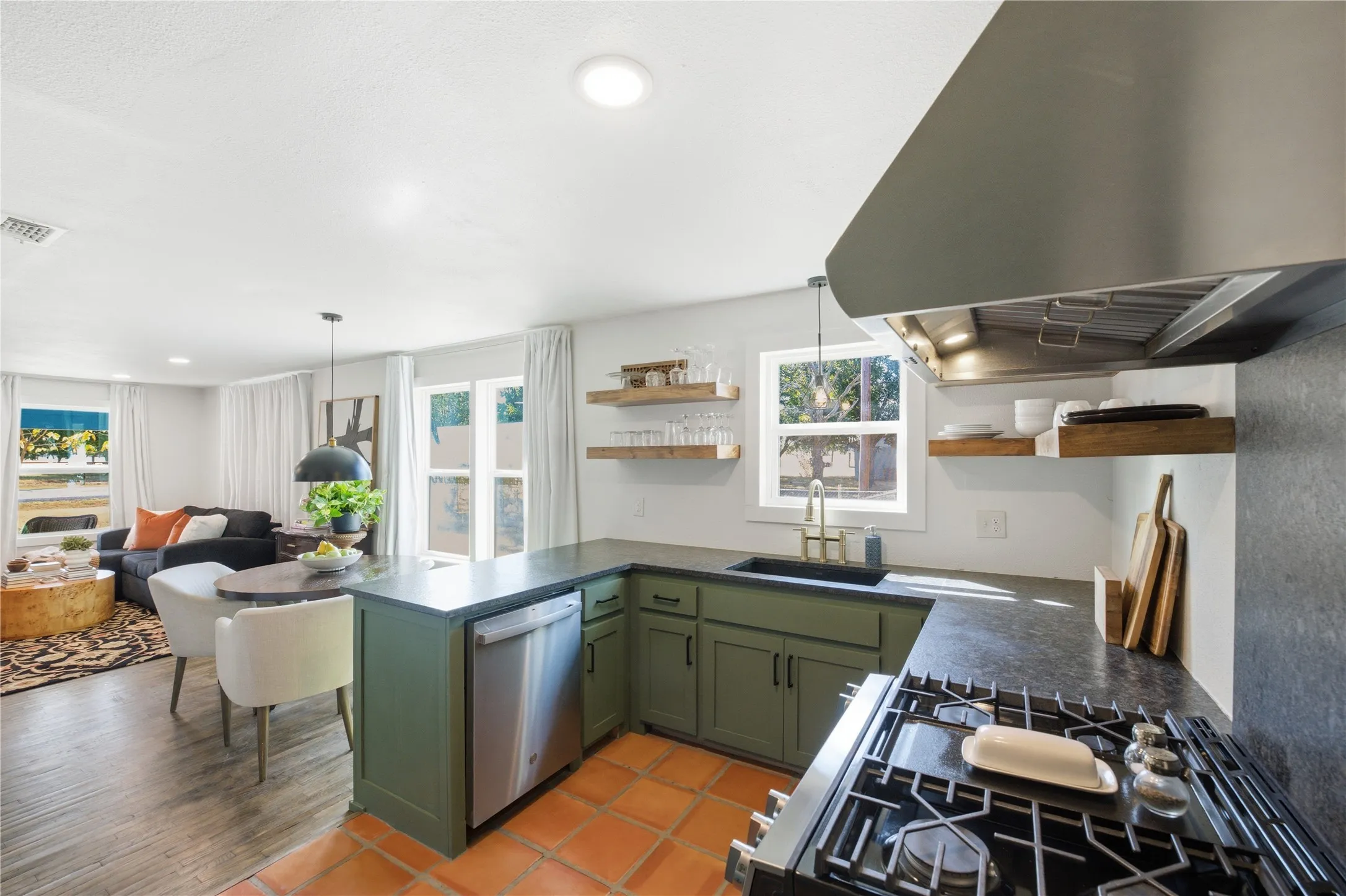 Kitchen featuring sage green cabinetry, dark countertops, a stainless steel gas range with a matching range hood, and open wood shelving