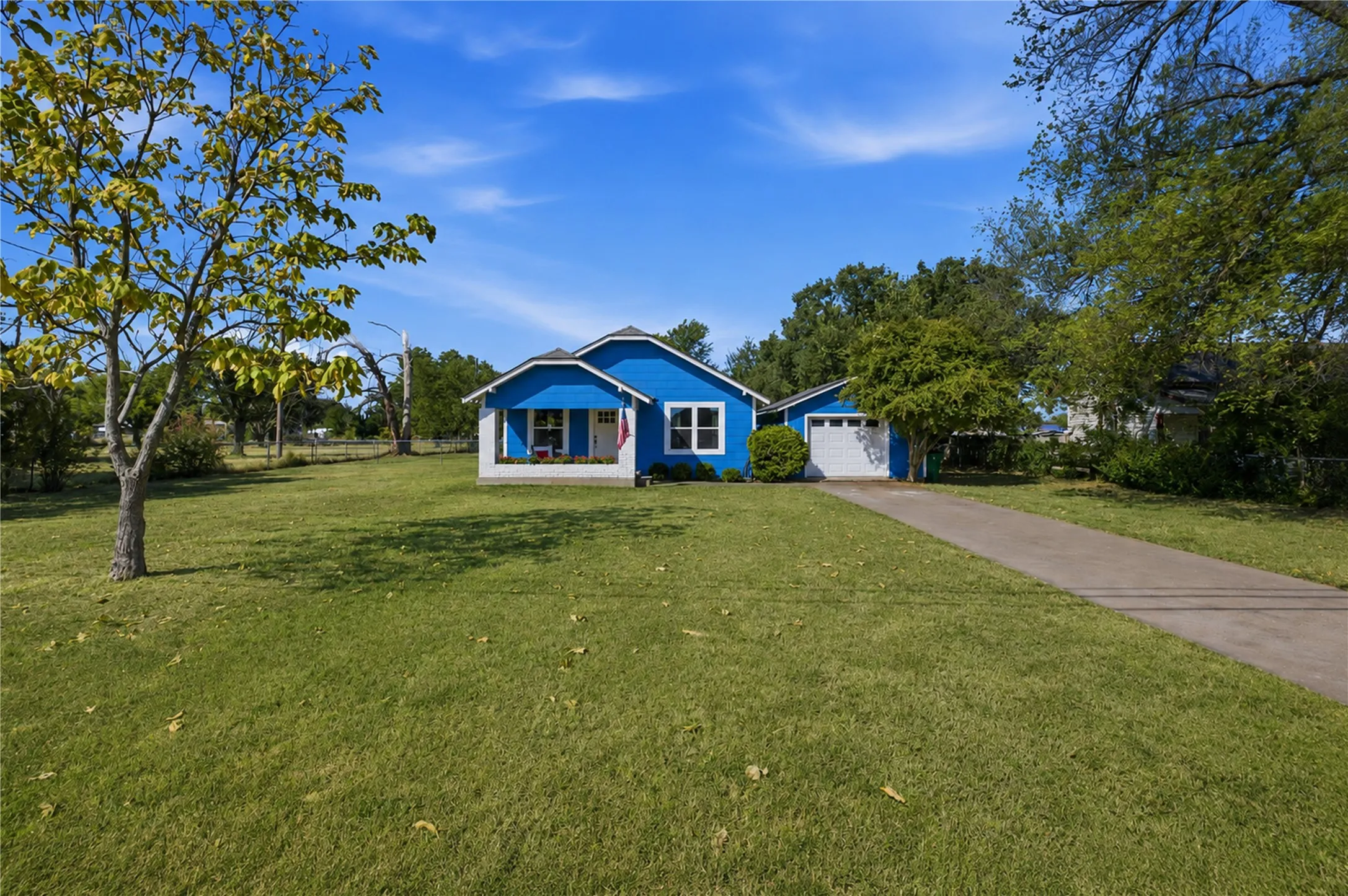 Vibrant blue exterior with a covered front porch, white trim, attached garage, and a concrete driveway