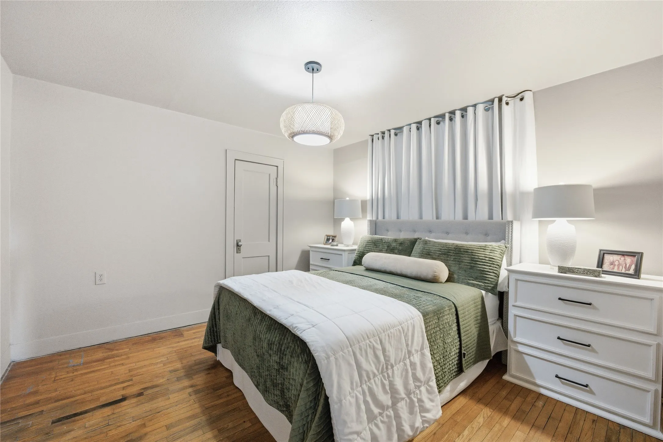 Hardwood flooring, white painted walls, white trim, white interior door, and a decorative pendant light fixture