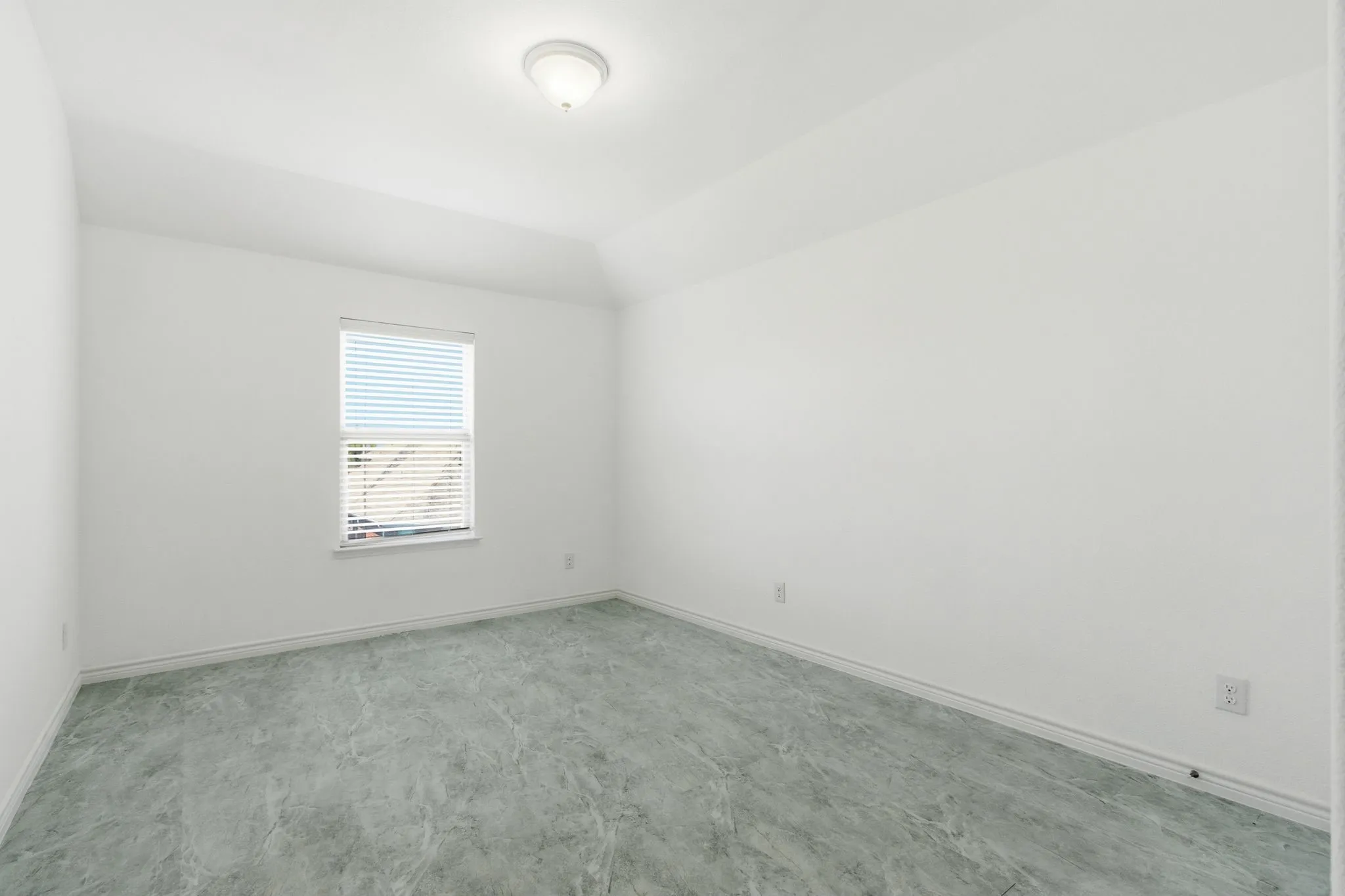 Vaulted ceiling, white walls, window with blinds, overhead flush-mount light fixture, and patterned gray flooring