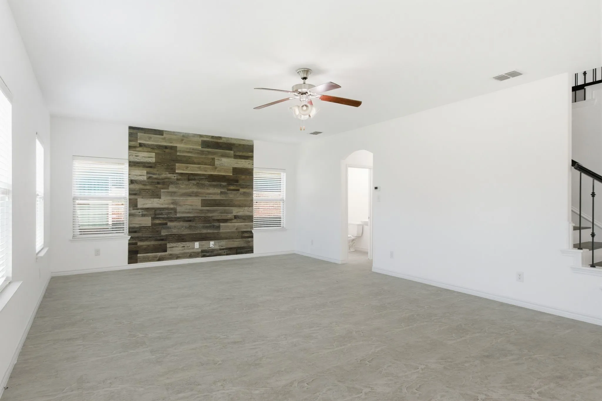 Spacious room featuring a decorative wood-panel accent wall, neutral carpeting, and multiple windows with blinds