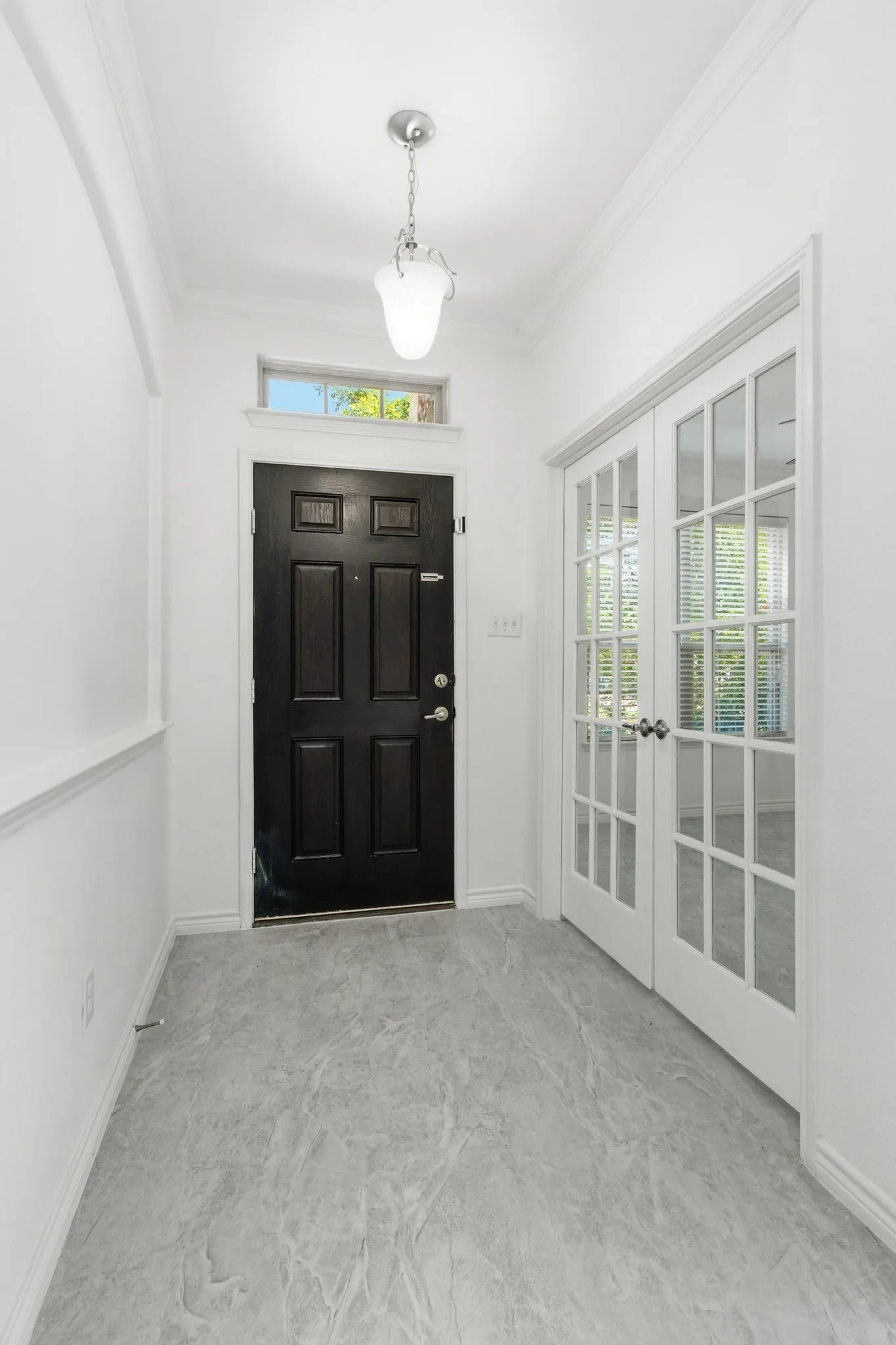 Entryway featuring a six-panel dark-finish door with transom window, gray-toned tile flooring, and white French doors