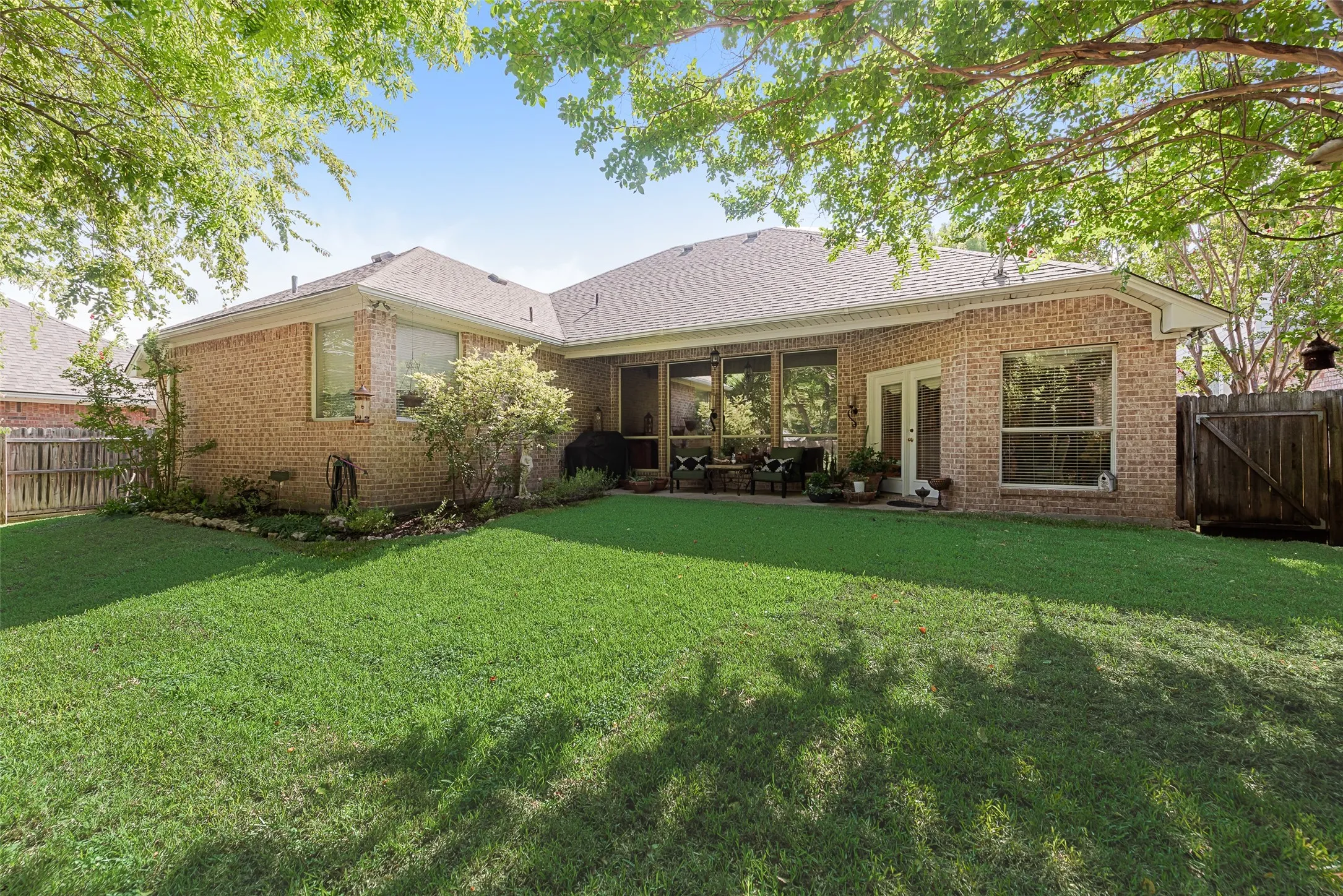 Expansive backyard featuring a manicured lawn, full brick exterior, double pane windows, wood fence, and a covered patio