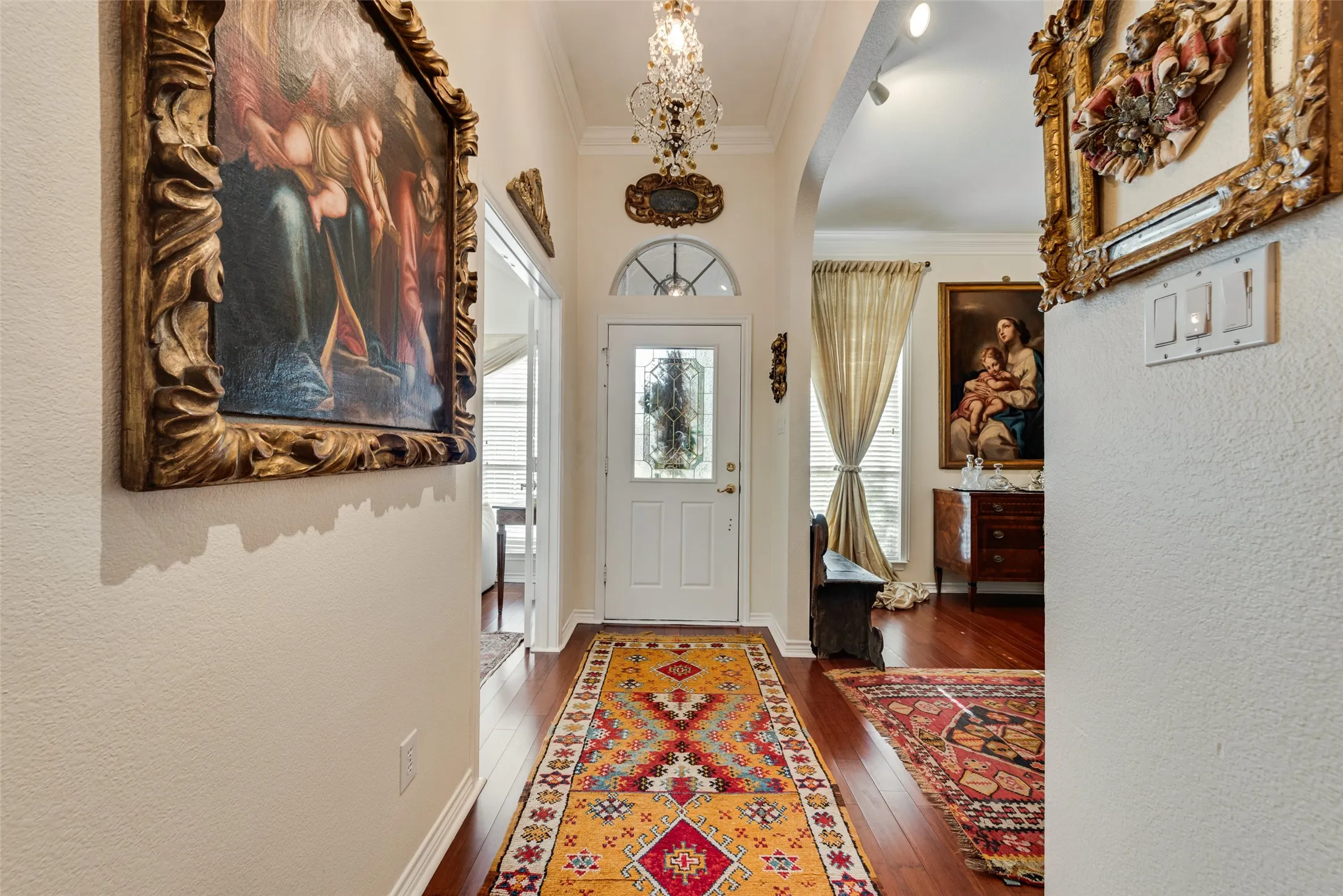 Arched entryway with a decorative glass door, wood-finish flooring, and crown molding