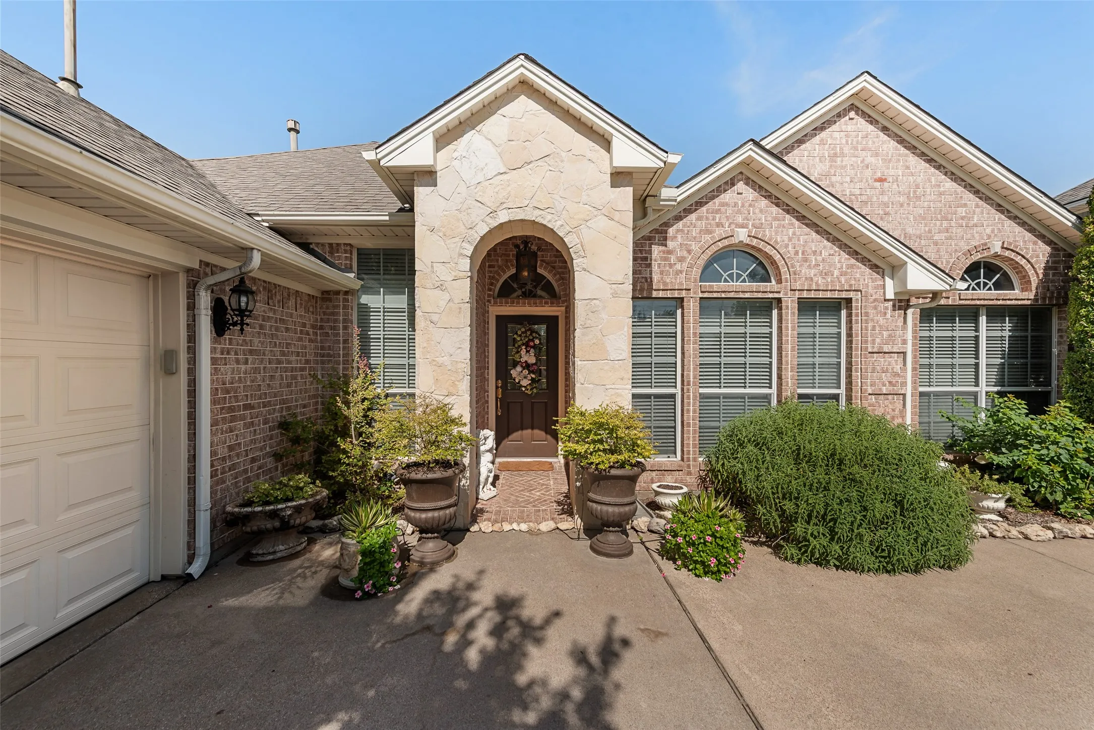 Brick and stone exterior featuring an arched entry, multiple arched windows, and an attached garage