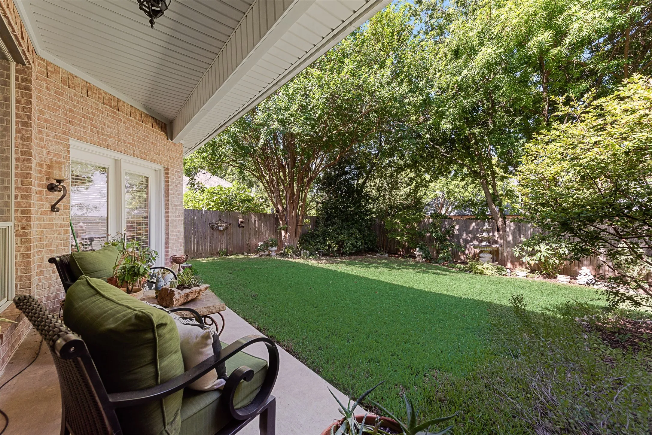 Covered patio with brick exterior, concrete flooring, and an expansive lawn