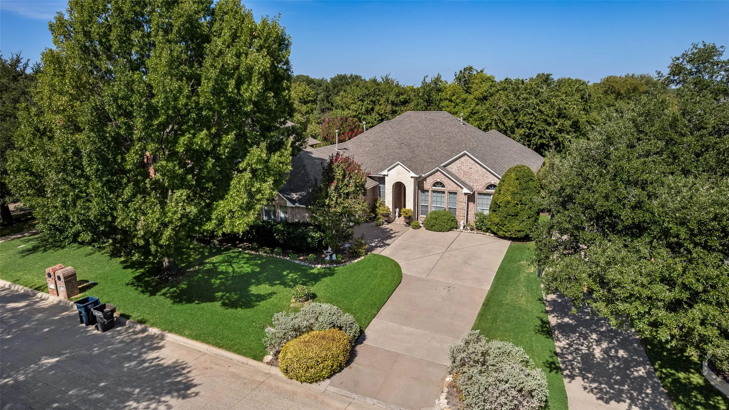 Brick exterior, arched entryway, bay windows, concrete driveway, mature trees