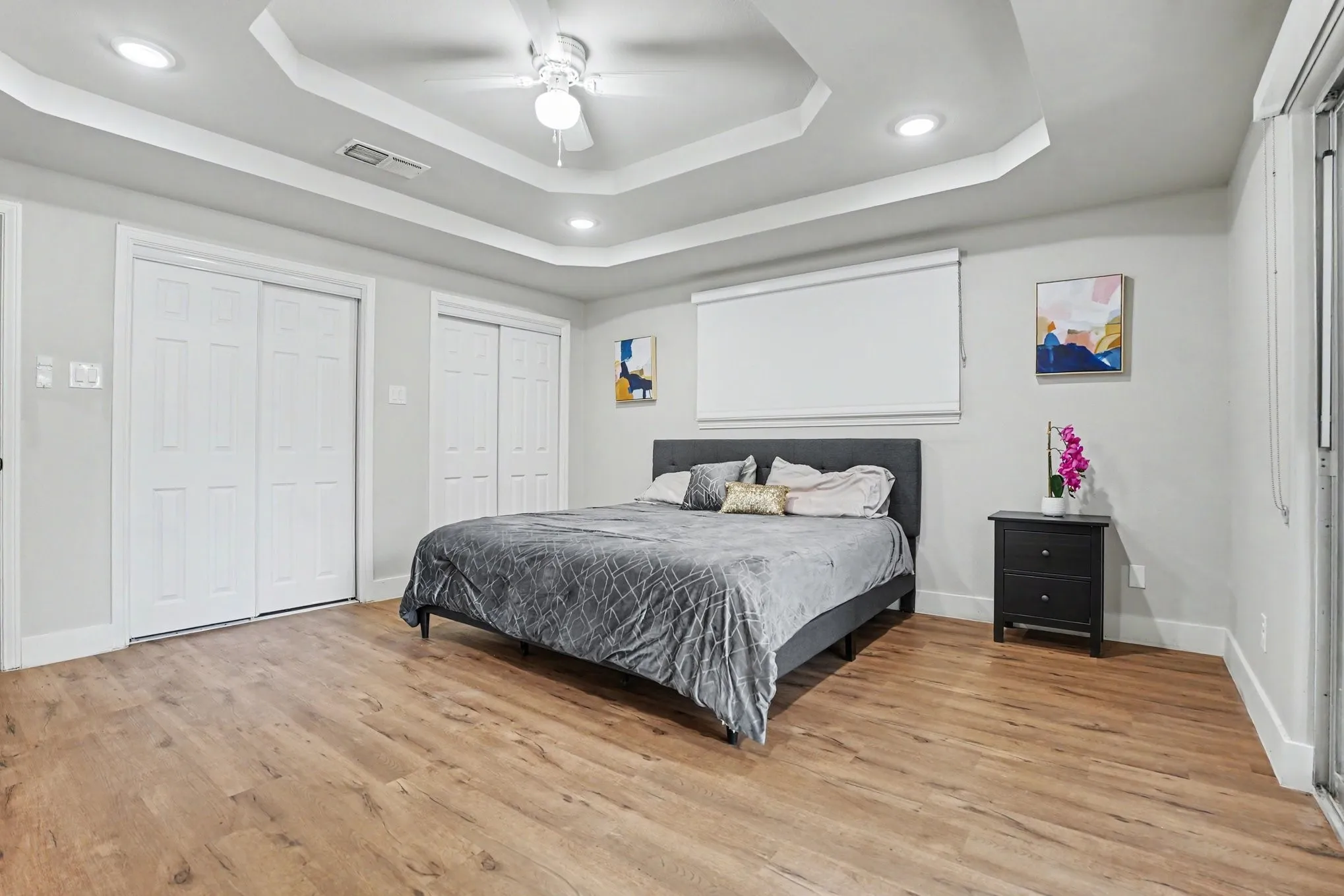 Tray ceiling with recessed lighting and ceiling fan, wood-finish flooring, and white bi-fold closet doors