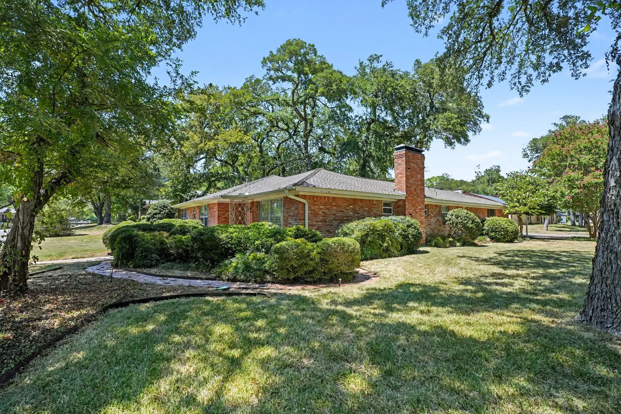 Brick exterior with a prominent brick chimney, surrounded by mature trees and established landscaping