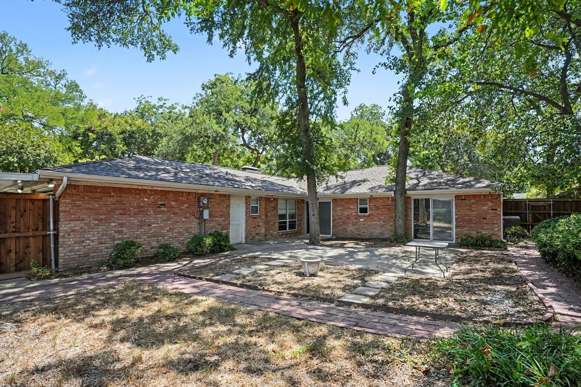 Brick exterior construction with a covered patio, paved walkway, and mature trees