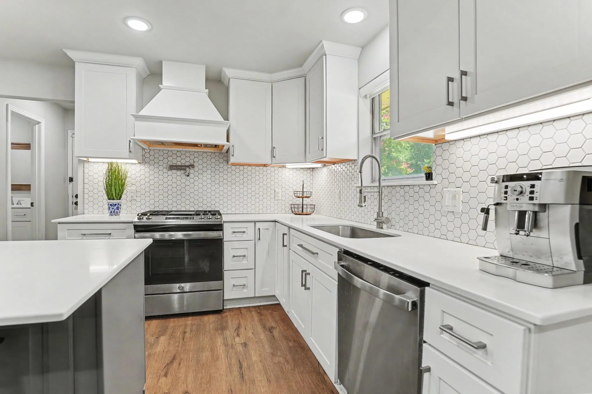 Contemporary kitchen featuring white cabinetry, stainless steel appliances, hexagon tile backsplash, and wood-finish flooring