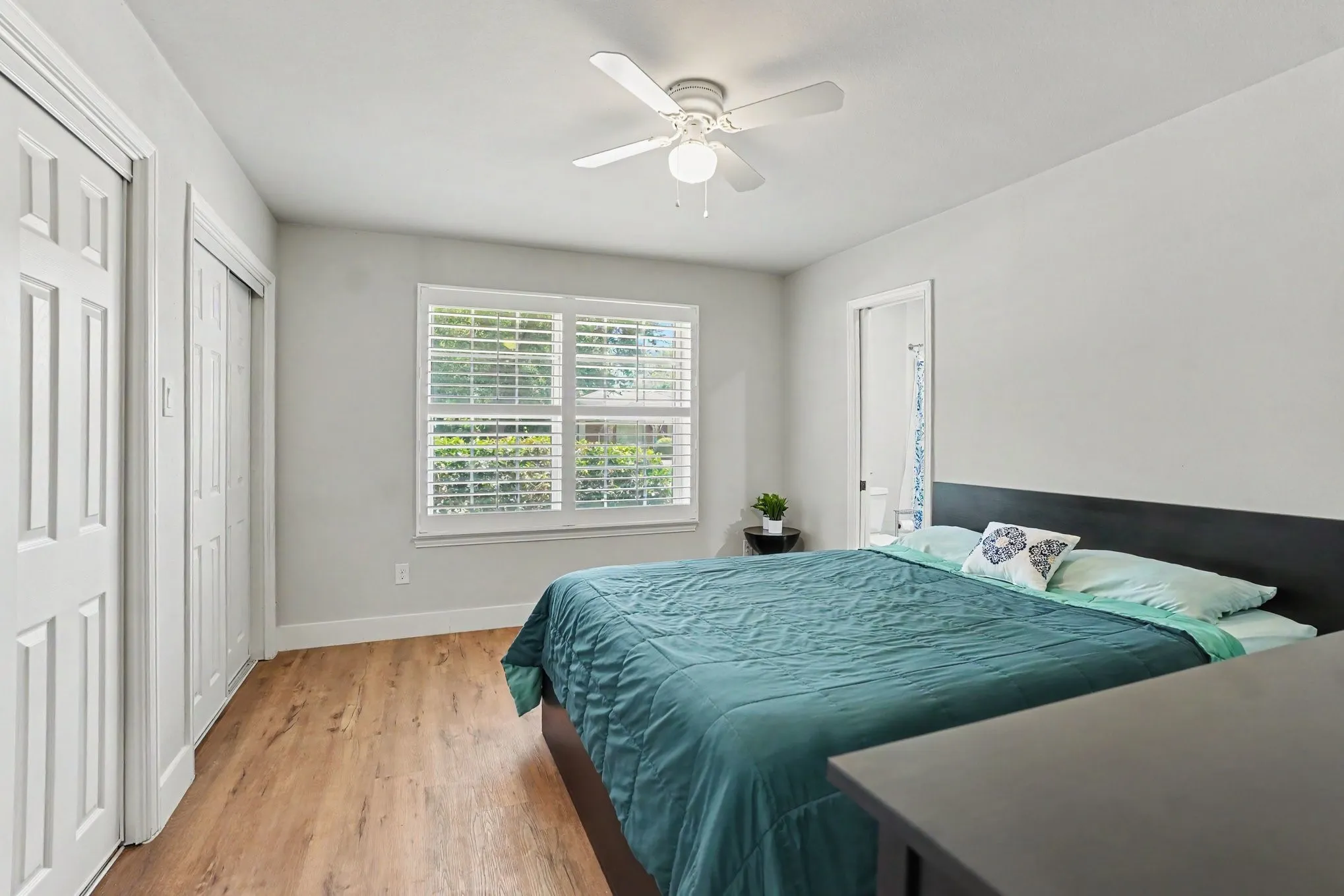 Wood-finish flooring, white plantation shutters, and a ceiling fan with light fixture