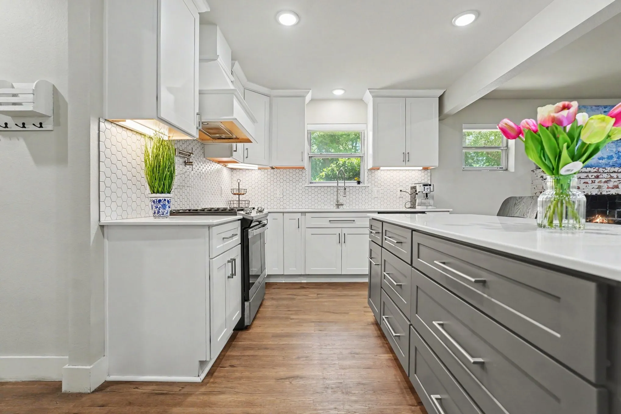 Contemporary kitchen featuring wood-finish flooring, white cabinetry, hexagon tile backsplash, recessed lighting, and a contrasting island with a light-colored countertop