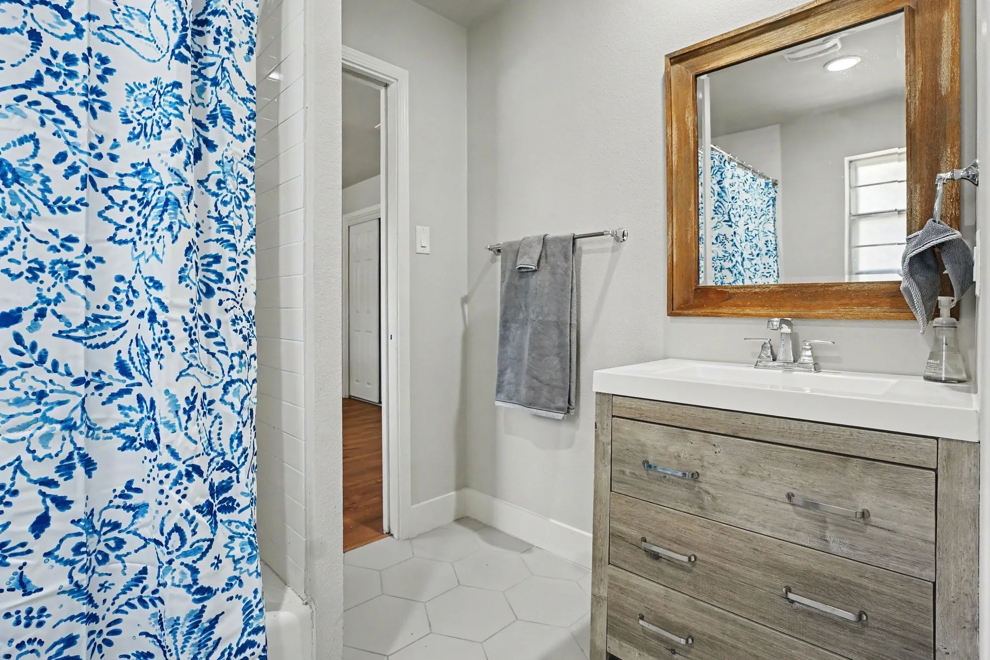 Hexagonal floor tiling, wood-finish vanity with drawer storage, integrated sink, chrome faucet, and a wood-framed mirror