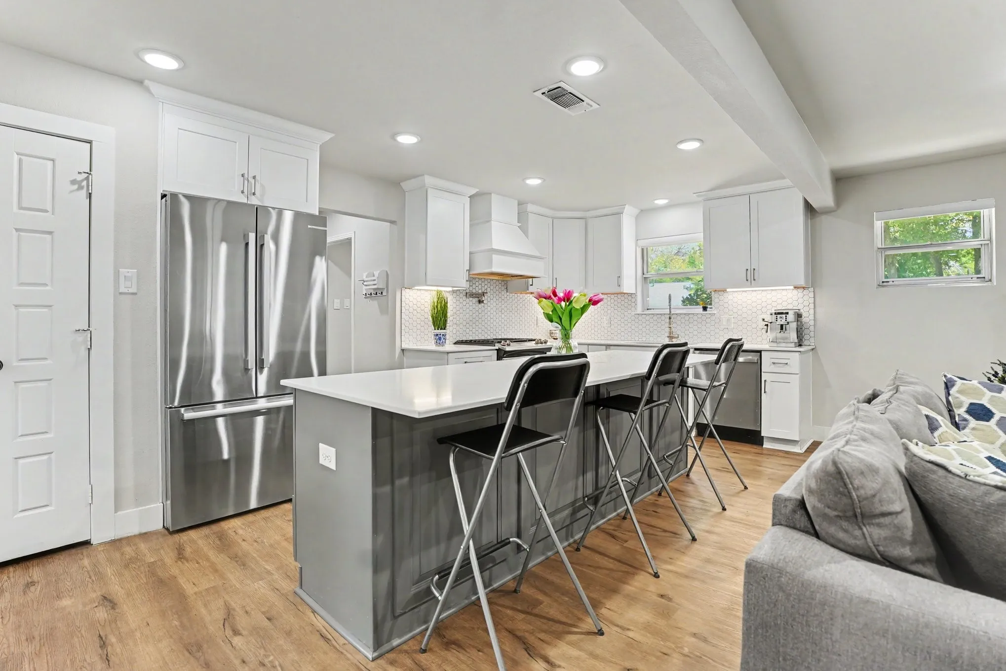 Kitchen featuring wood-finish flooring, recessed lighting, white shaker-style cabinetry, a white tile backsplash, and a large center island with a light-colored countertop