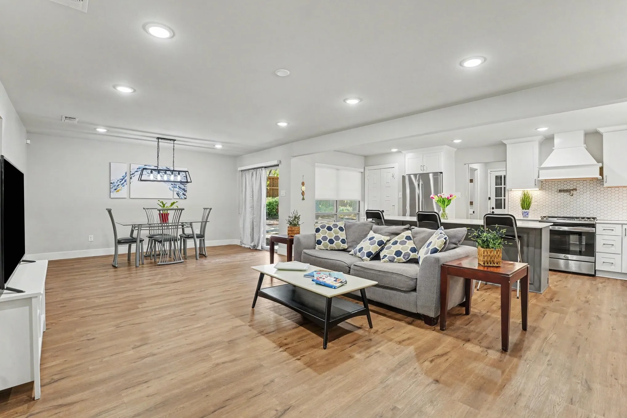Open-concept living space featuring wood-finish flooring, recessed lighting, and a modern kitchen with a hexagonal tile backsplash and stainless steel appliances
