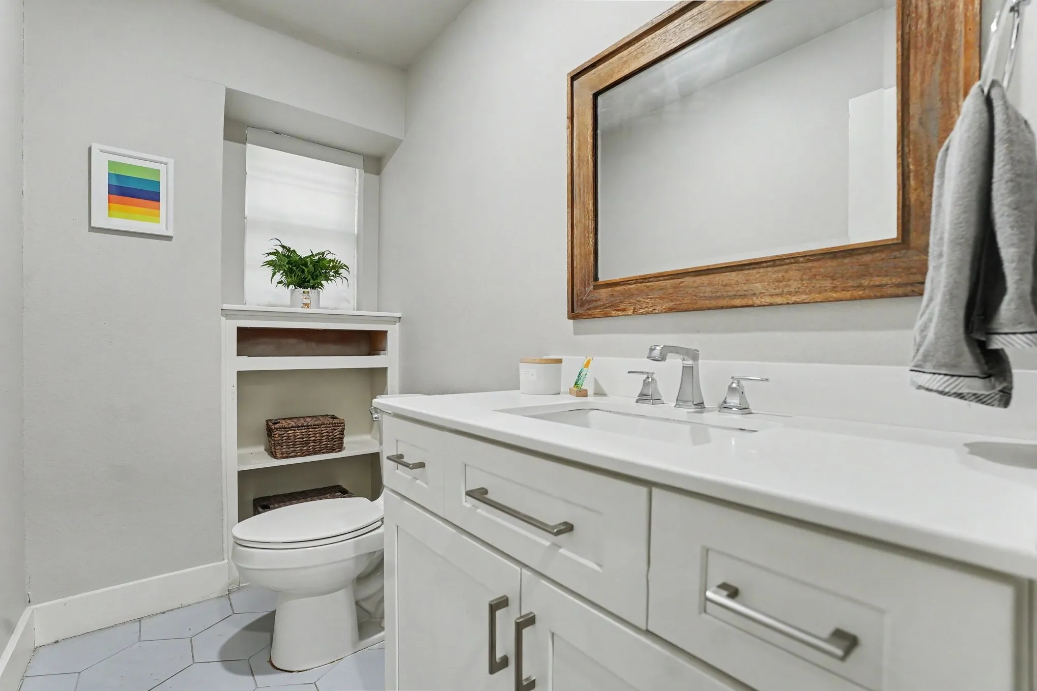 Hexagonal floor tiling, built-in shelving, white vanity with polished hardware, white countertop, and a wood-framed mirror