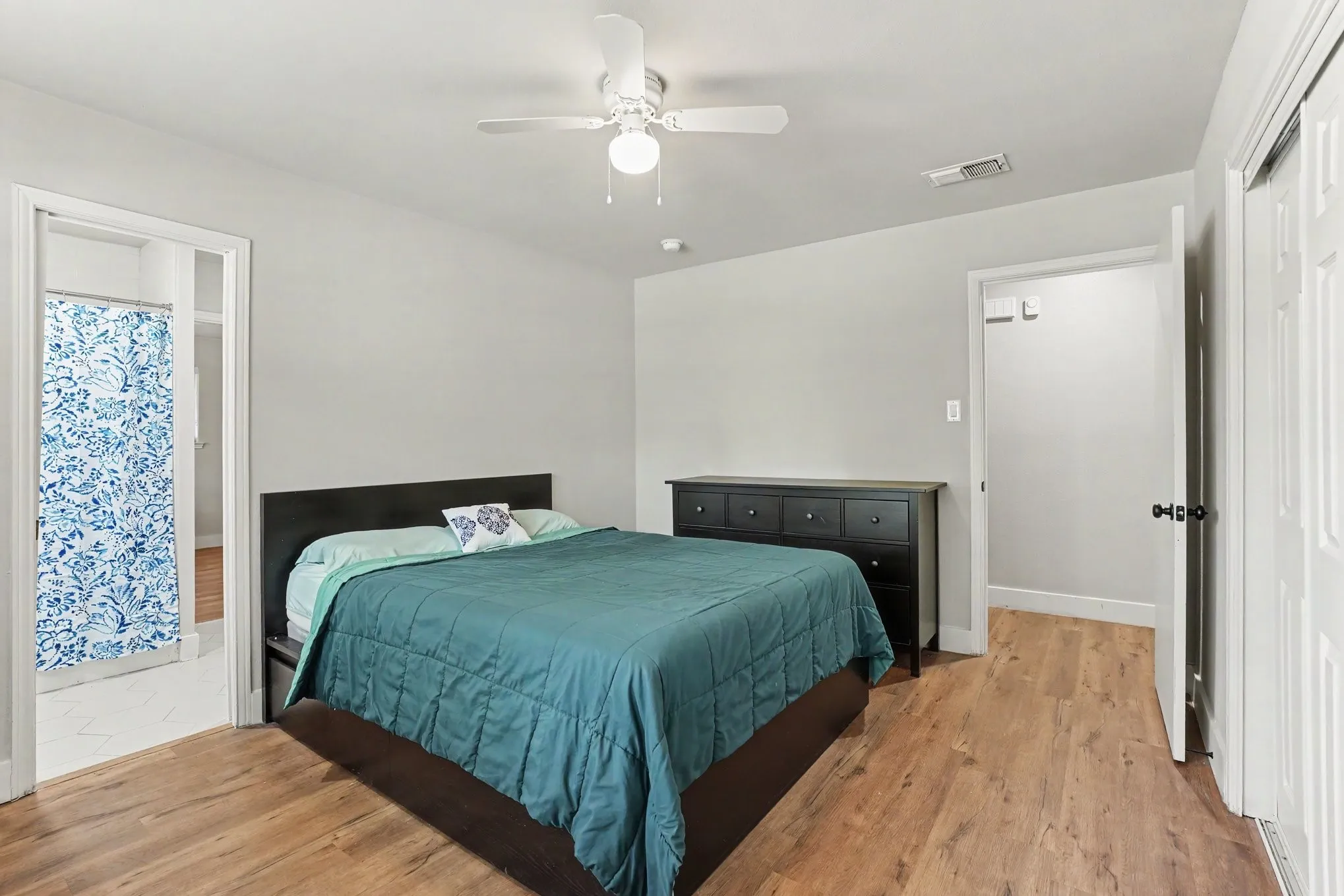 Light gray wall paint, wood-finish flooring, white ceiling fan, white paneled doors, and an open doorway to an adjoining room