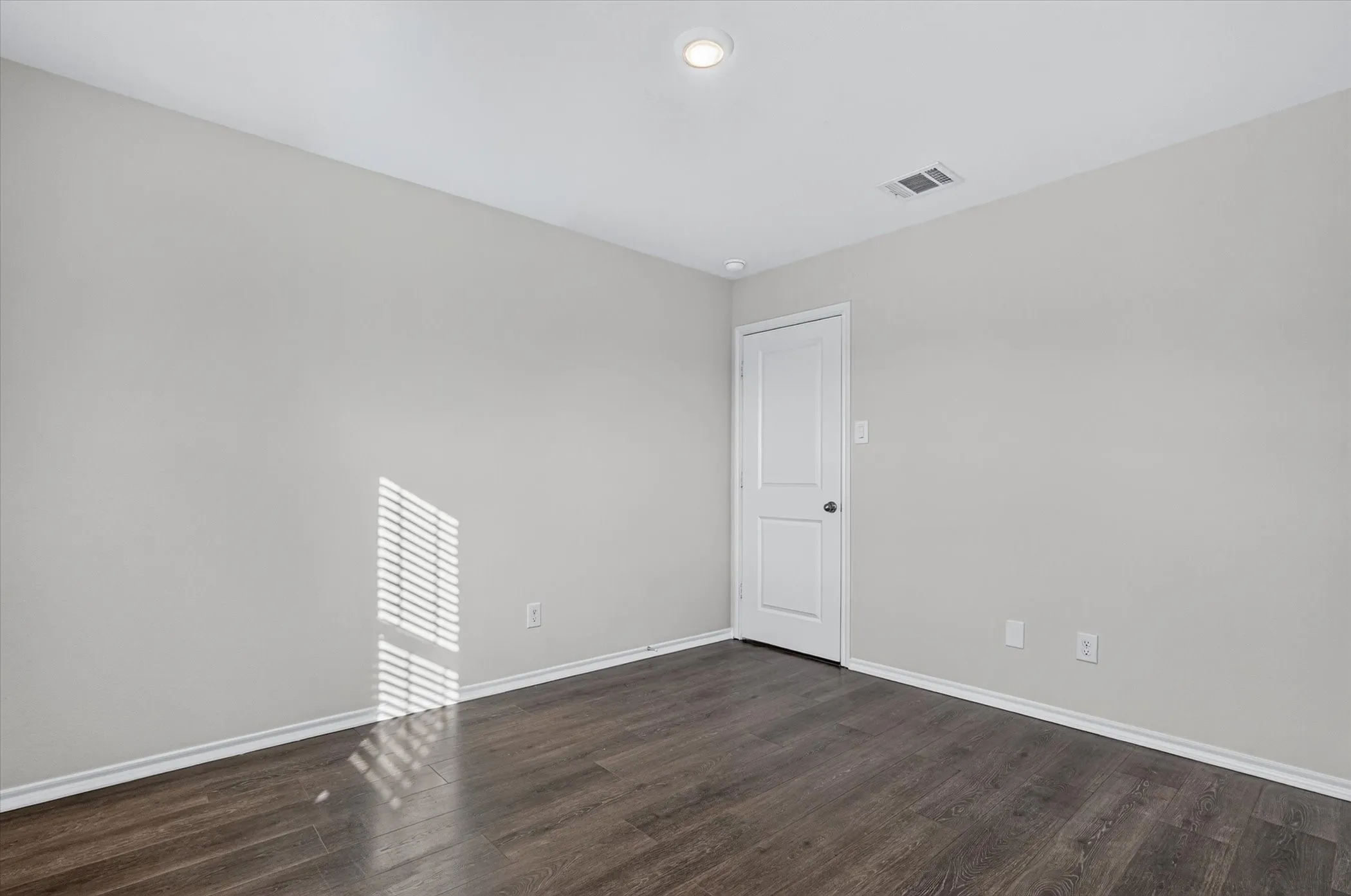 Recessed ceiling lighting, wood-finish flooring, light neutral wall paint, white trim, and a paneled interior door