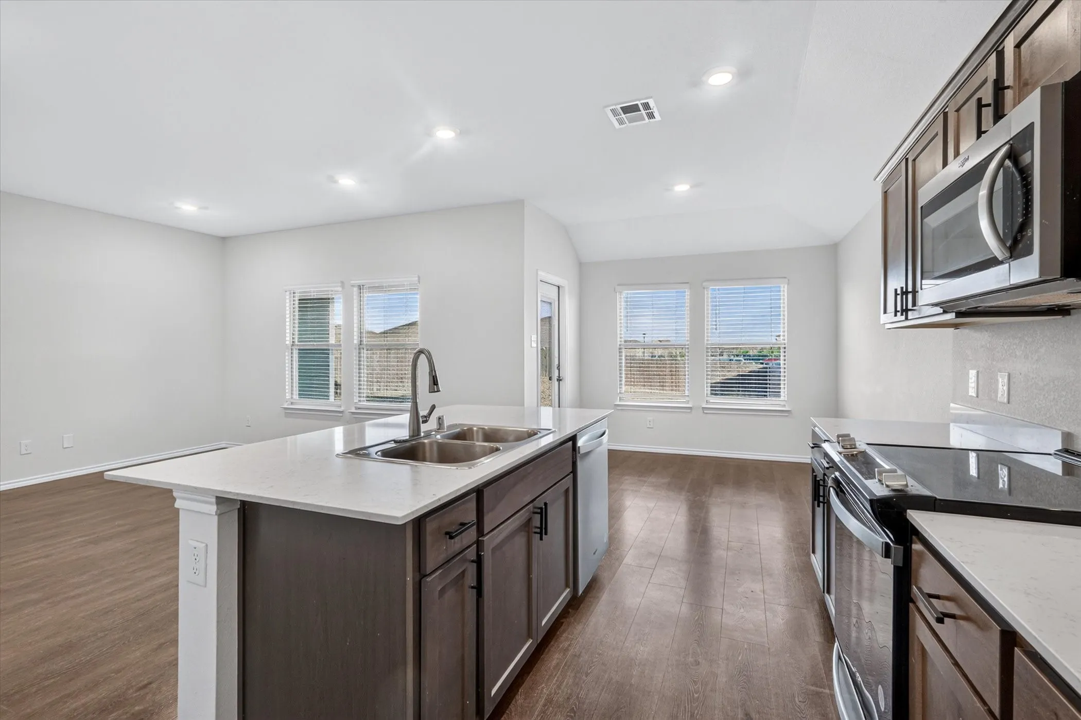 Kitchen island with a double basin sink, stainless steel appliances, dark wood-finish cabinetry, and wood-finish flooring
