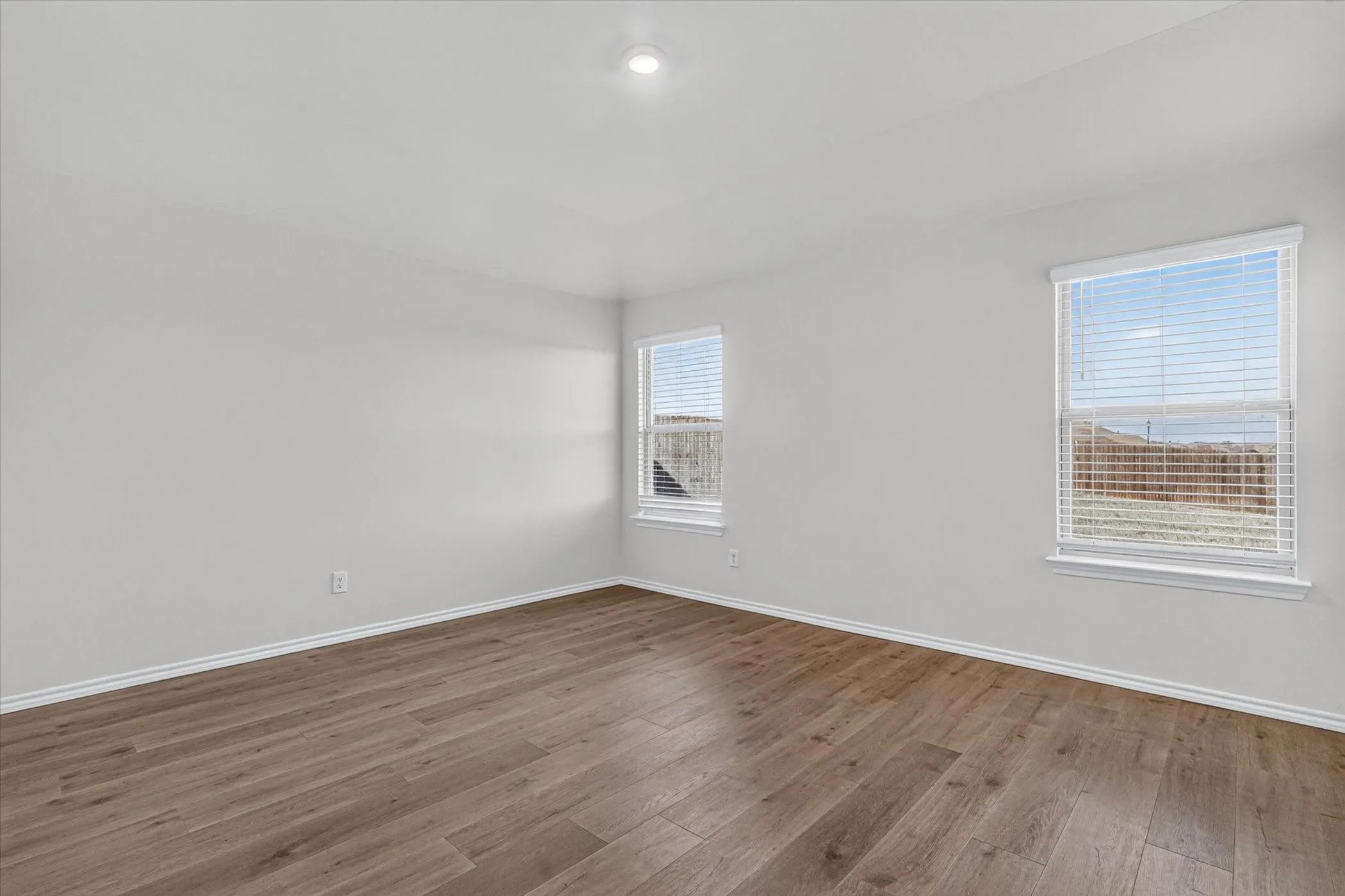 Recessed ceiling lighting, two windows with blinds, wood-finish flooring, and white trim