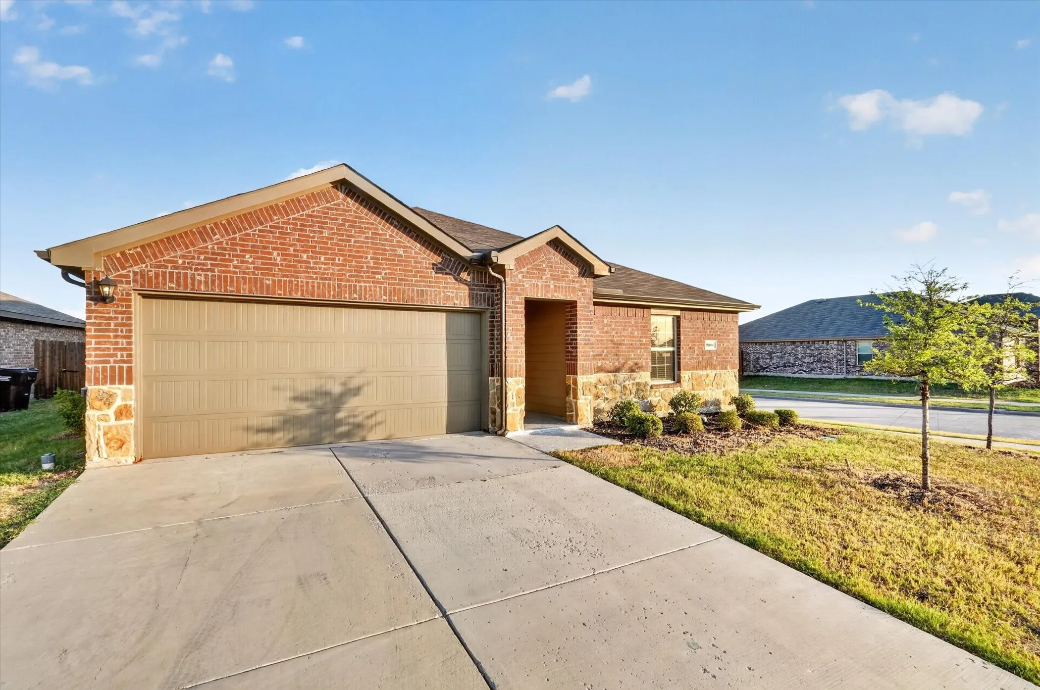 Brick and stone exterior with an attached garage, concrete driveway, and front landscaping