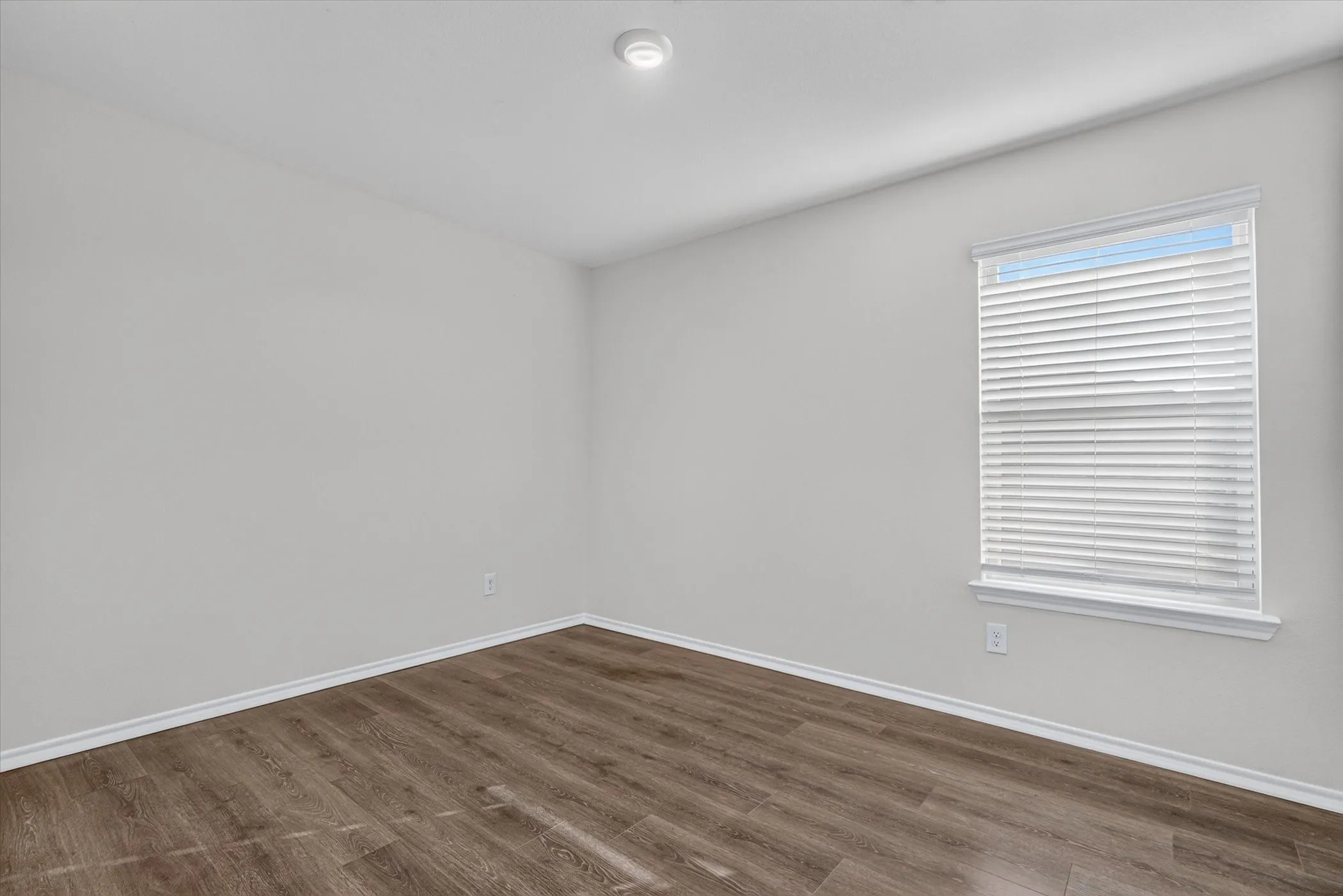 Wood-finish flooring, white baseboards, and a window with blinds