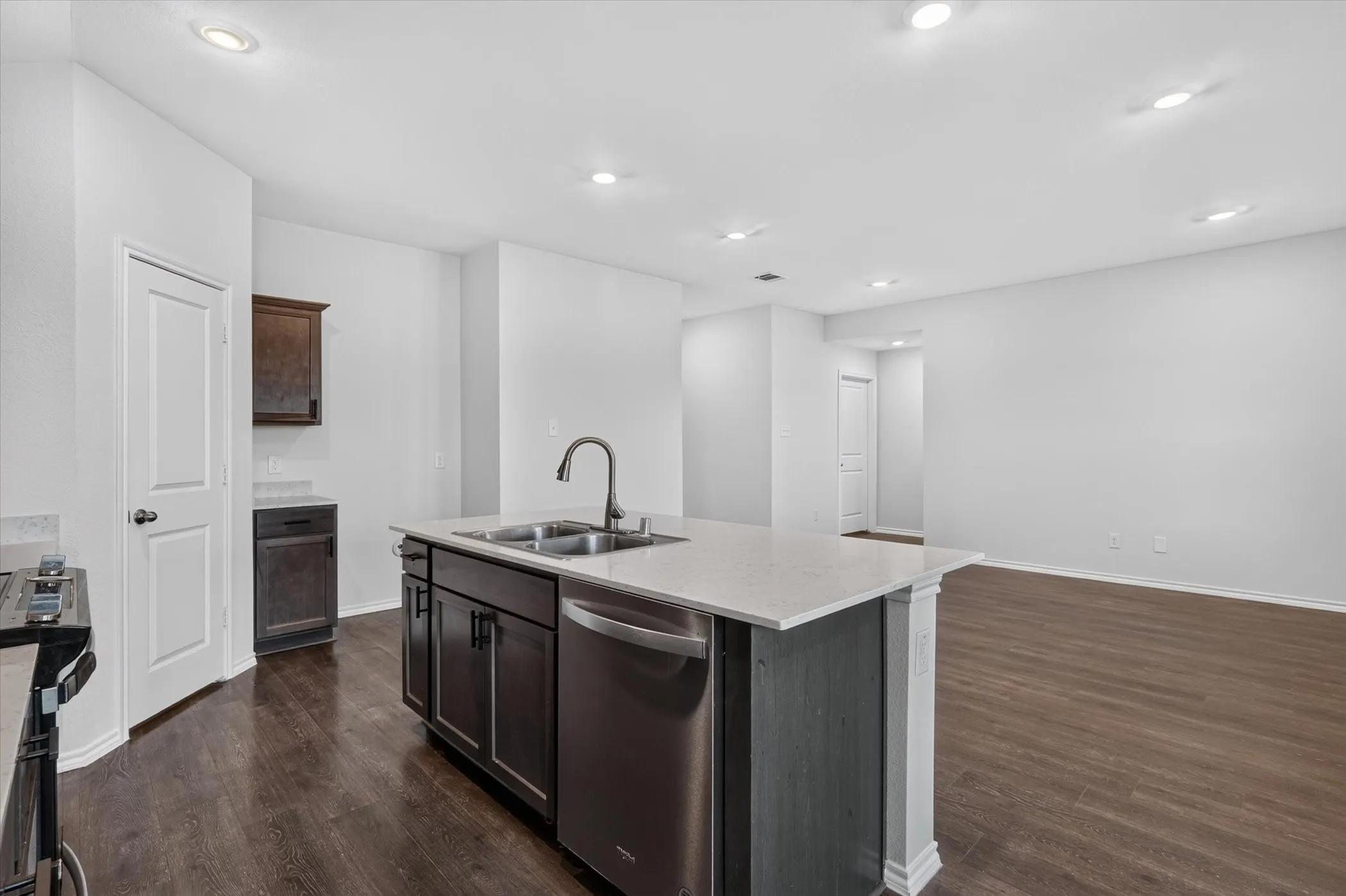 Open-concept kitchen featuring an island with a double basin sink, stainless steel dishwasher, and light-toned countertops