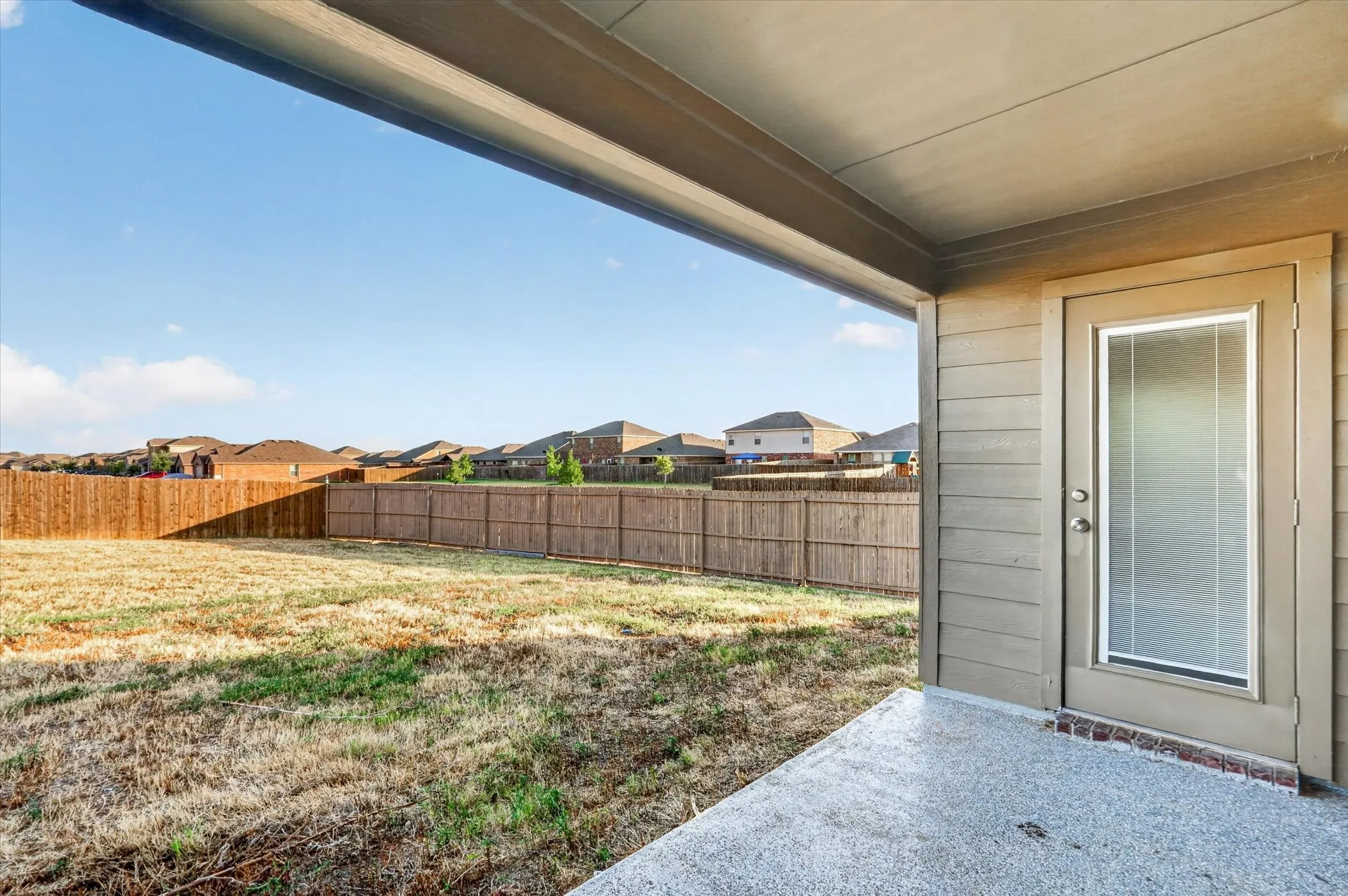 Spacious covered patio with concrete flooring overlooking a large fenced backyard with mature landscaping