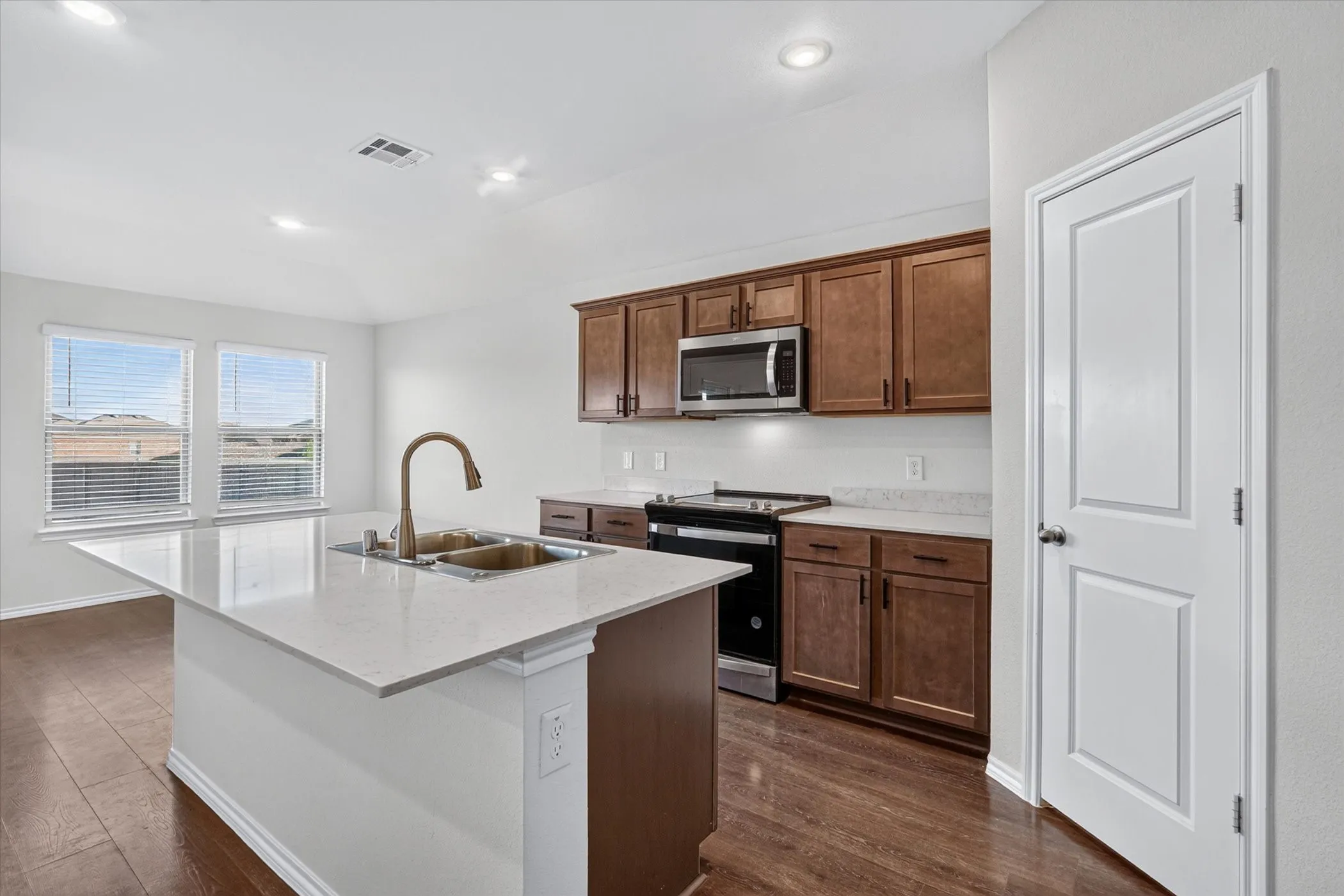 Kitchen featuring a central island with an undermount sink, wood-finish flooring, and two windows with blinds