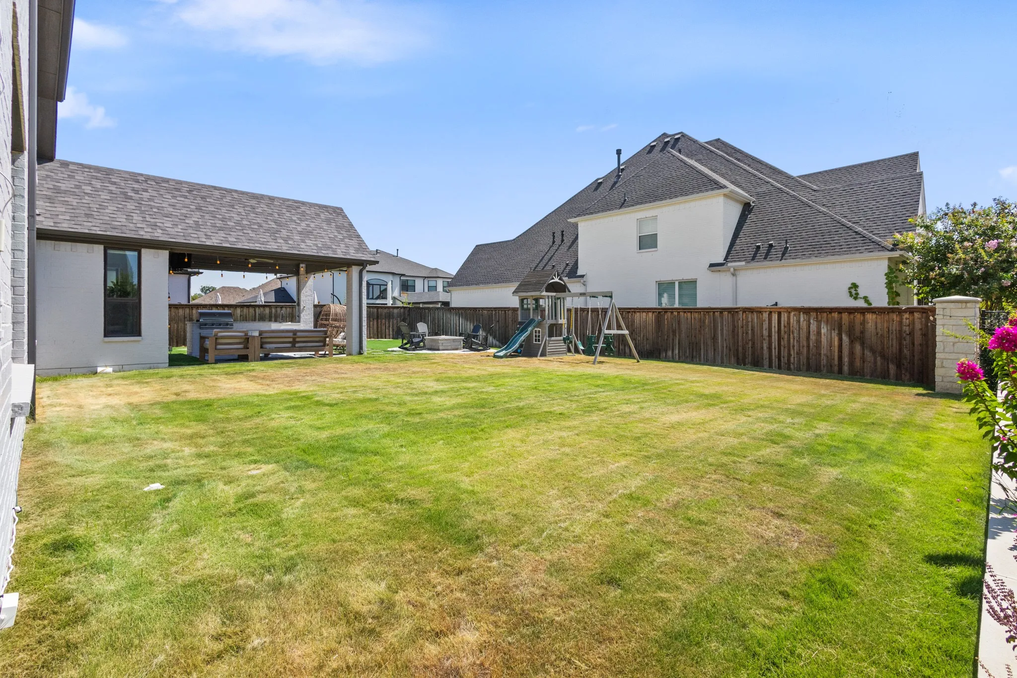 Spacious backyard with a covered patio, dark shingle roof, wood privacy fencing, and exterior lighting