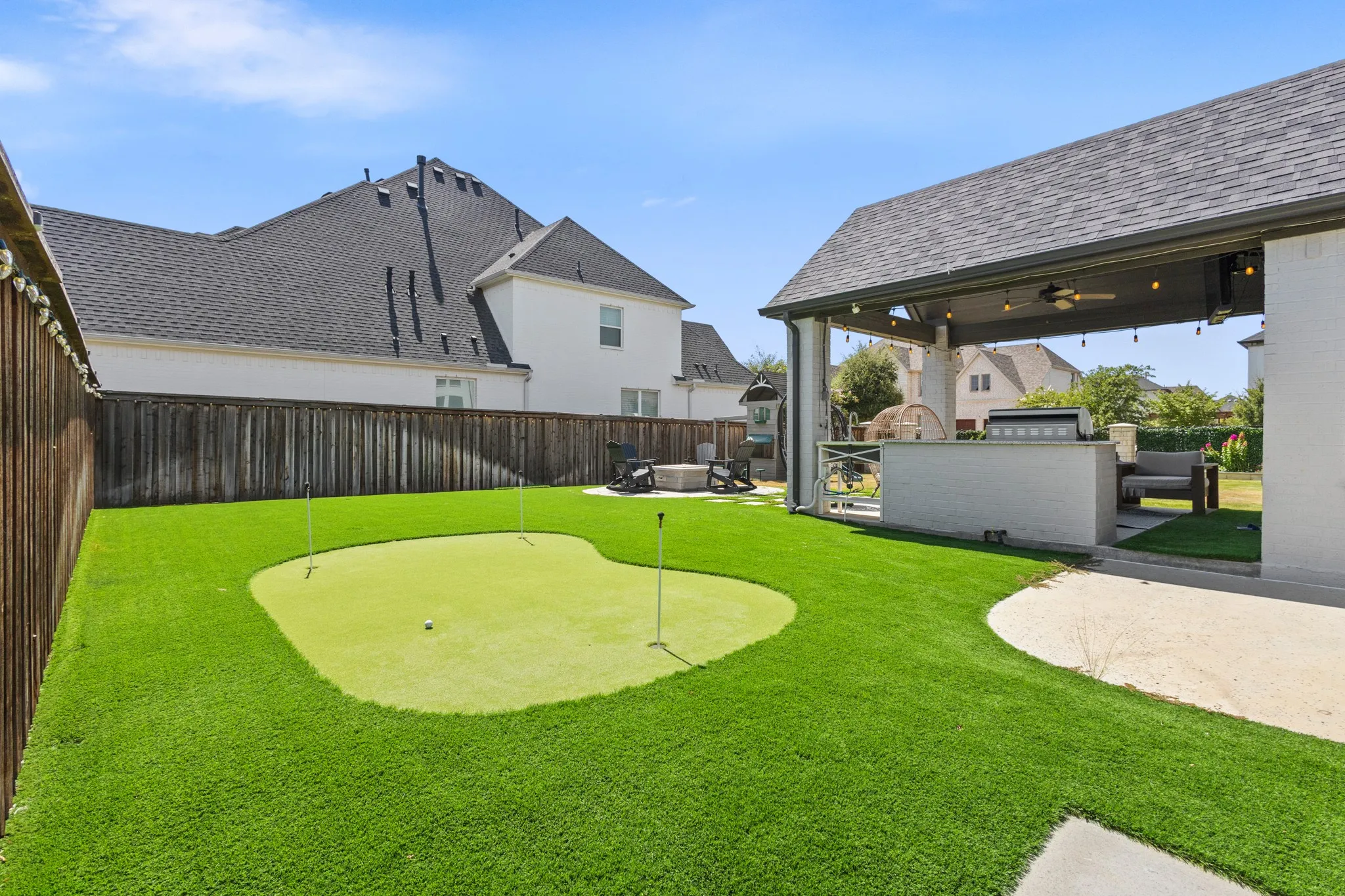 Covered patio with integrated outdoor kitchen, artificial turf, and a putting green