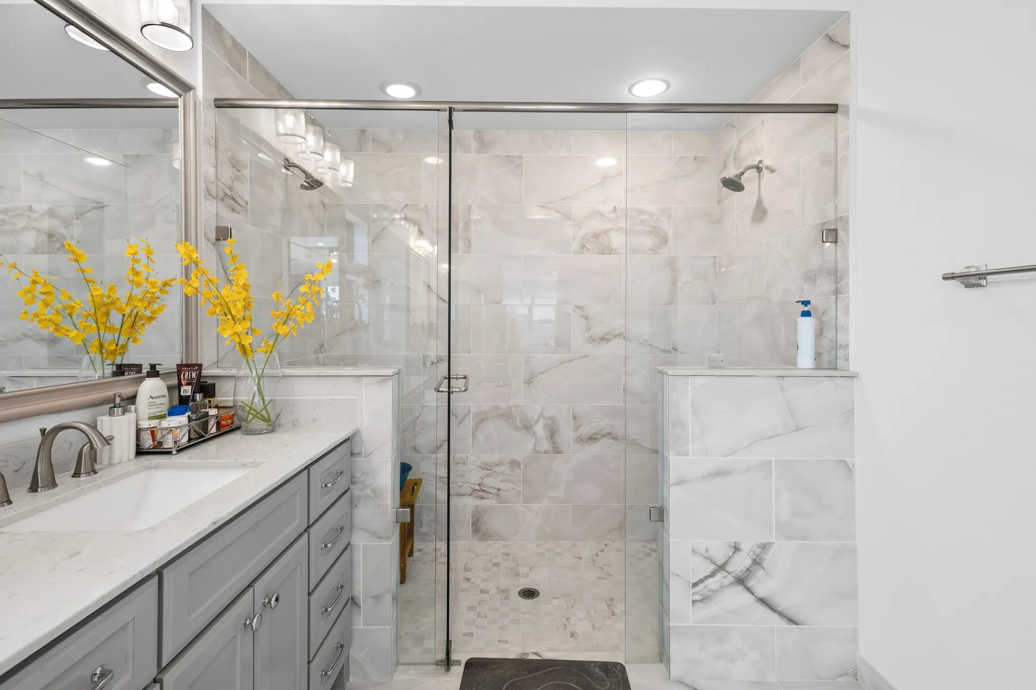 Glass-enclosed shower with dual shower heads, large format wall tile, and a built-in shower bench