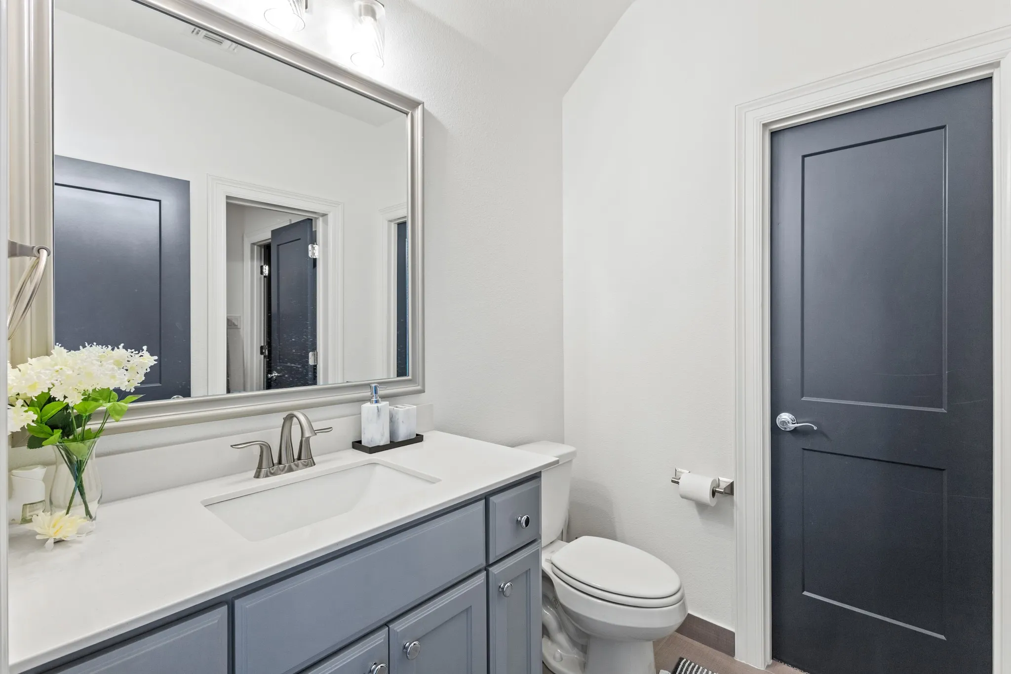 Single vanity with light gray cabinetry, white countertop, brushed nickel faucet, and a large framed mirror