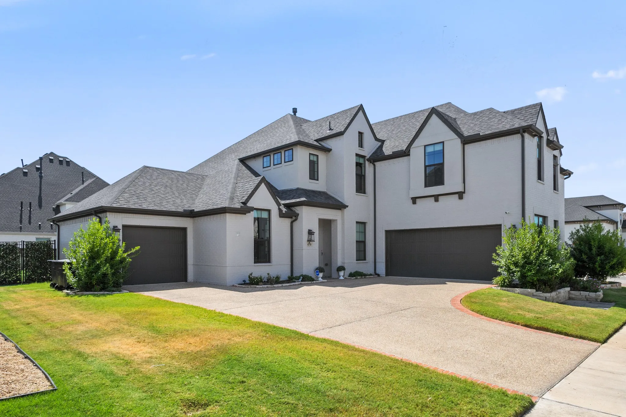 Stucco exterior with dark trim accents, multi-gabled roofline, multiple attached garages, and a concrete driveway