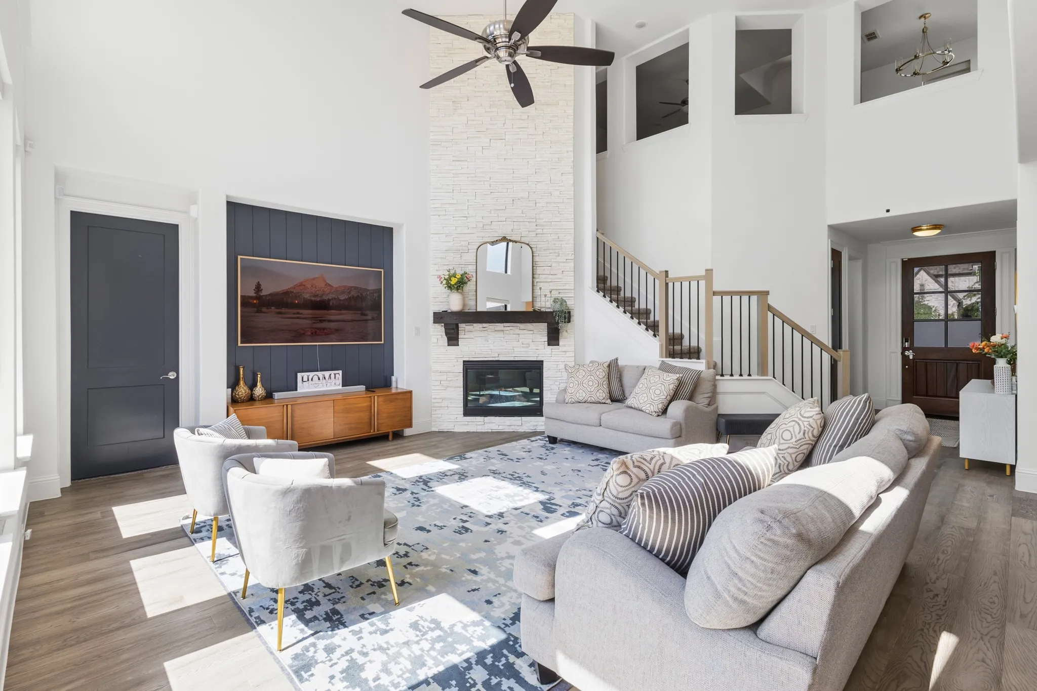 Two-story interior with a stone-finish fireplace, built-in electric fireplace, recessed ceiling fan, and wood-finish flooring