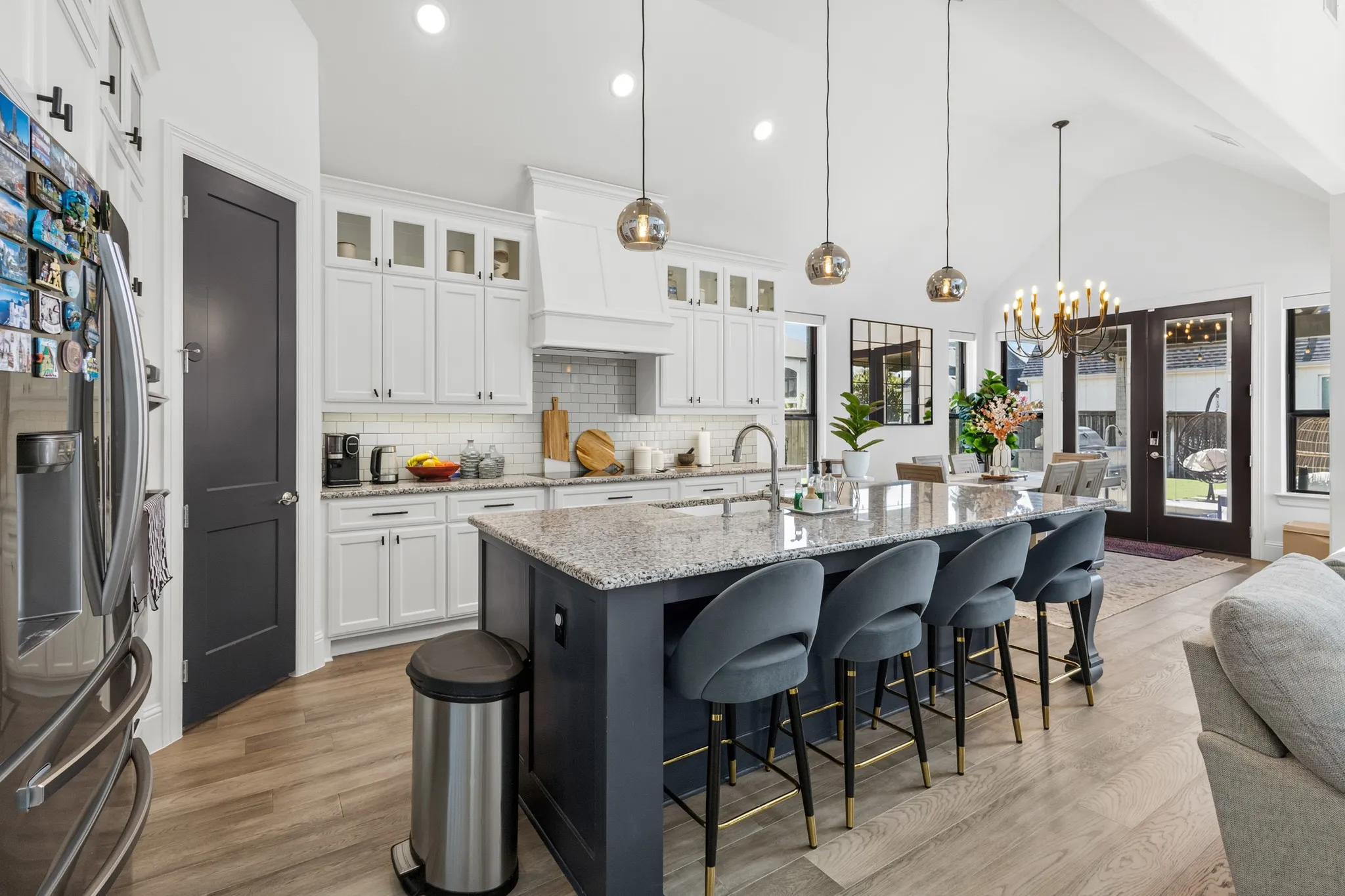 Spacious kitchen featuring an island with stone countertops, white shaker cabinetry, stainless steel appliances, and wood-finish flooring