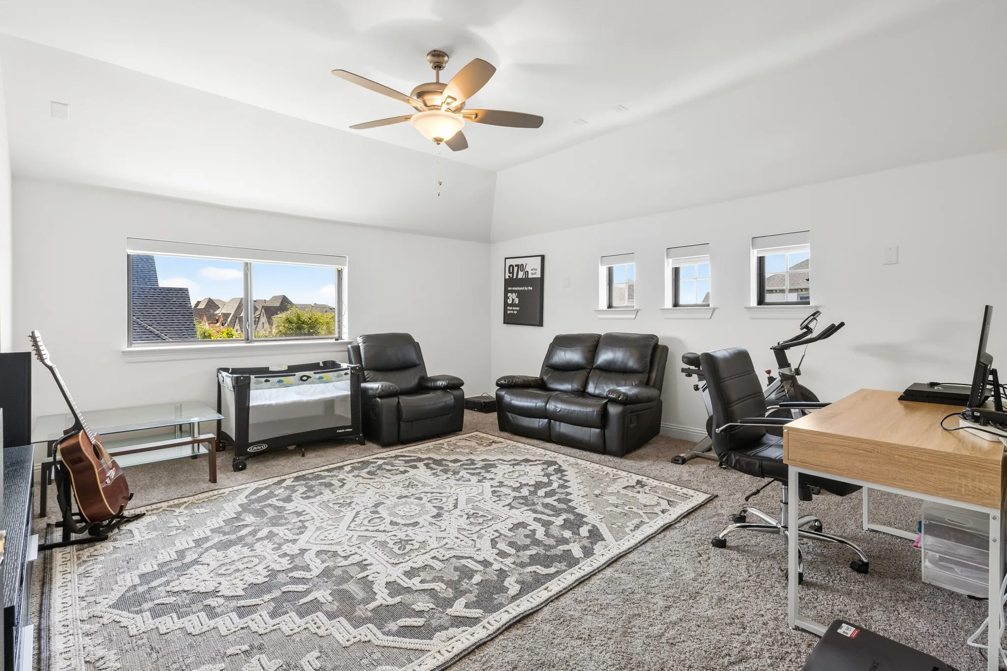 Spacious room featuring a vaulted ceiling with a ceiling fan, carpet flooring, a large window, and three smaller windows