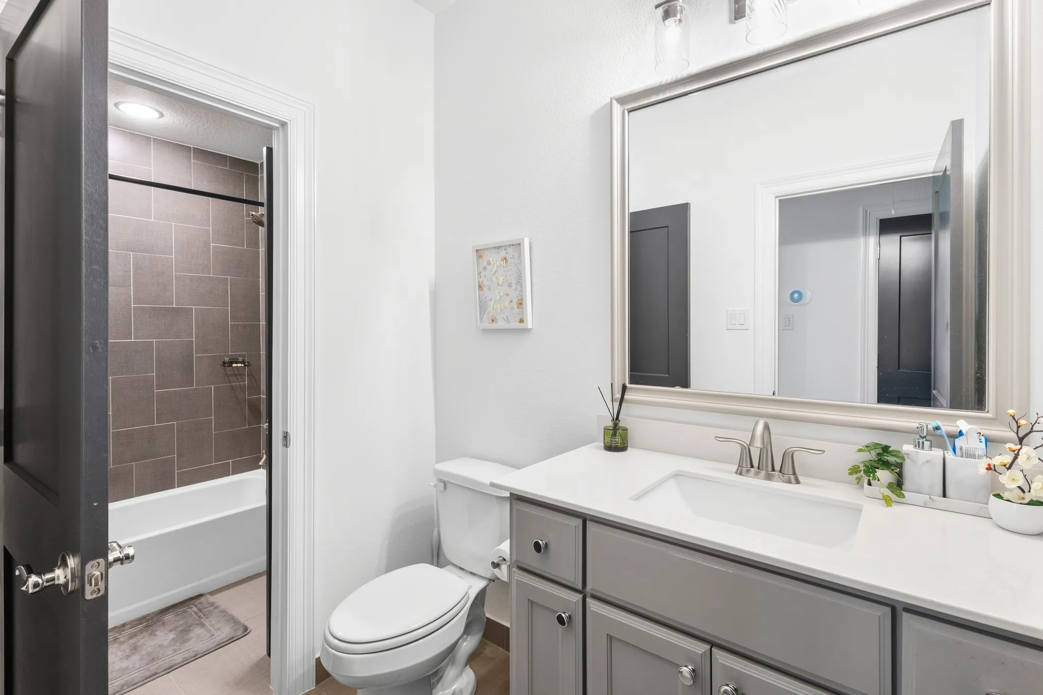 Vanity with a white countertop and undermount sink, framed mirror, and tile-surround bathtub