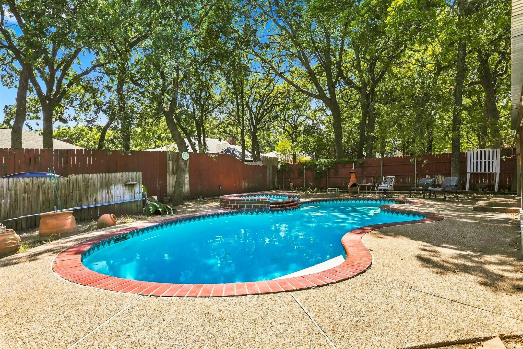 Free form swimming pool with a brick coping, integrated spa, and expansive aggregate concrete decking