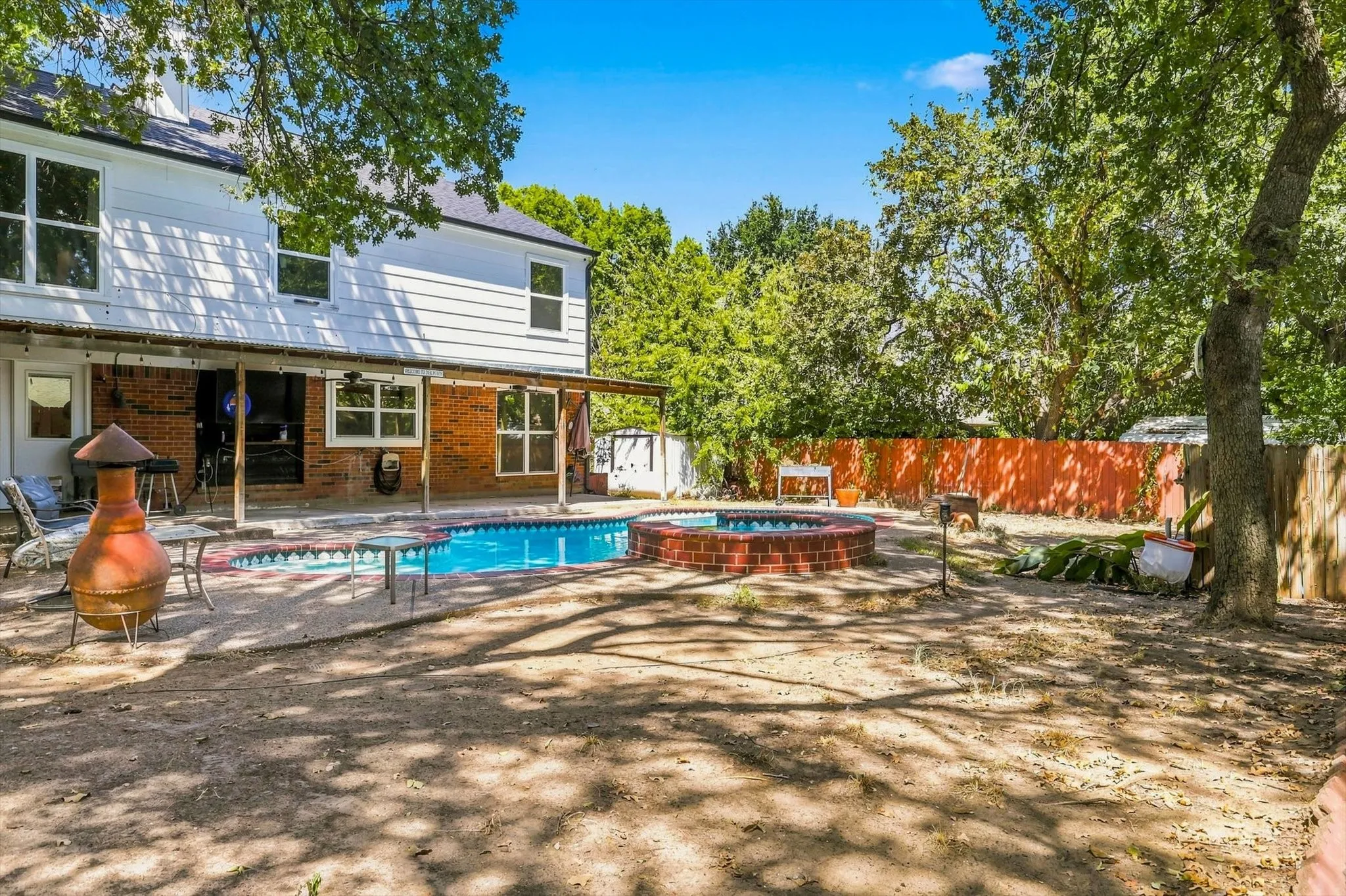 Expansive backyard featuring a swimming pool, a brick-edged hot tub, and a covered patio with exposed beams