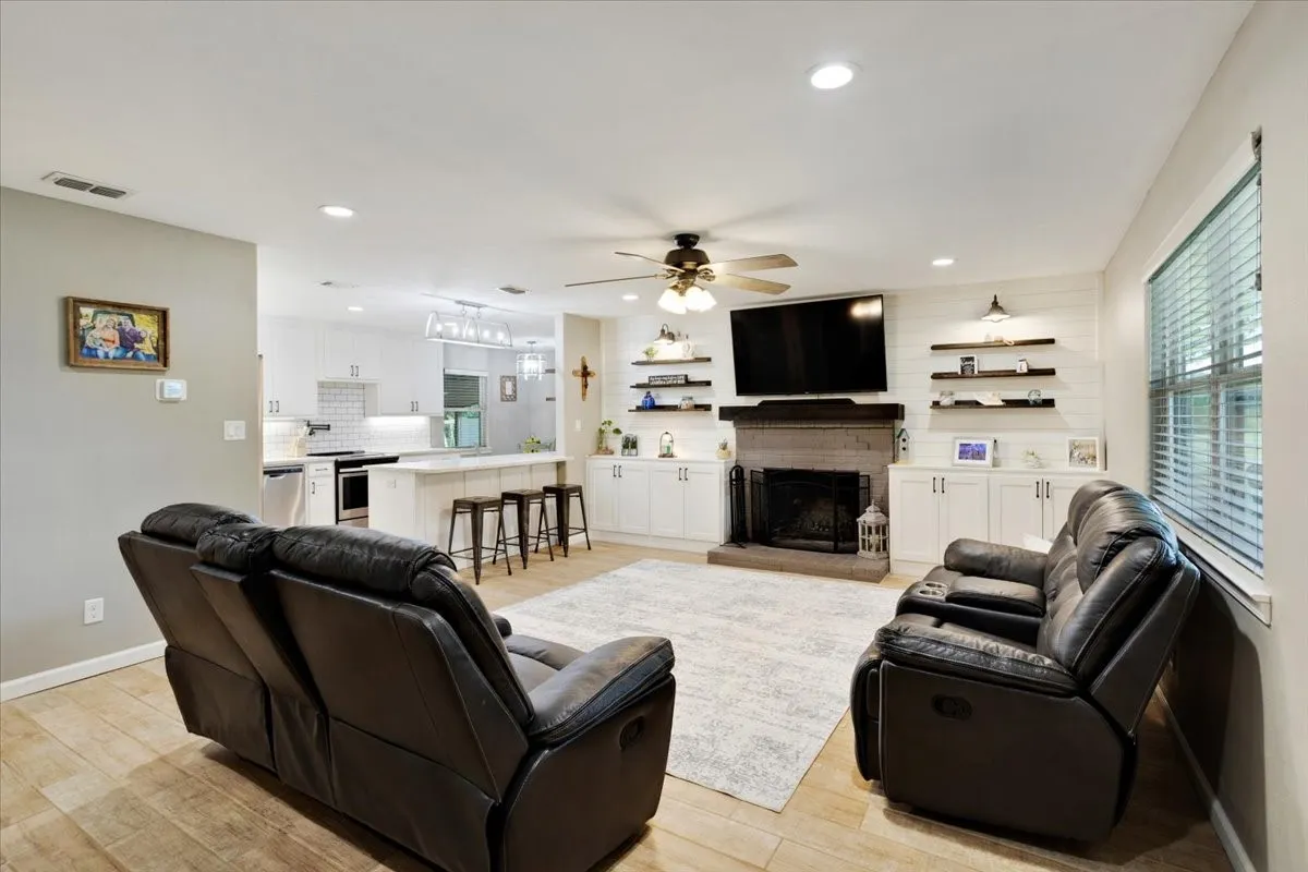 Open-concept living space with wood-finish flooring, a stone fireplace, and built-in shelving