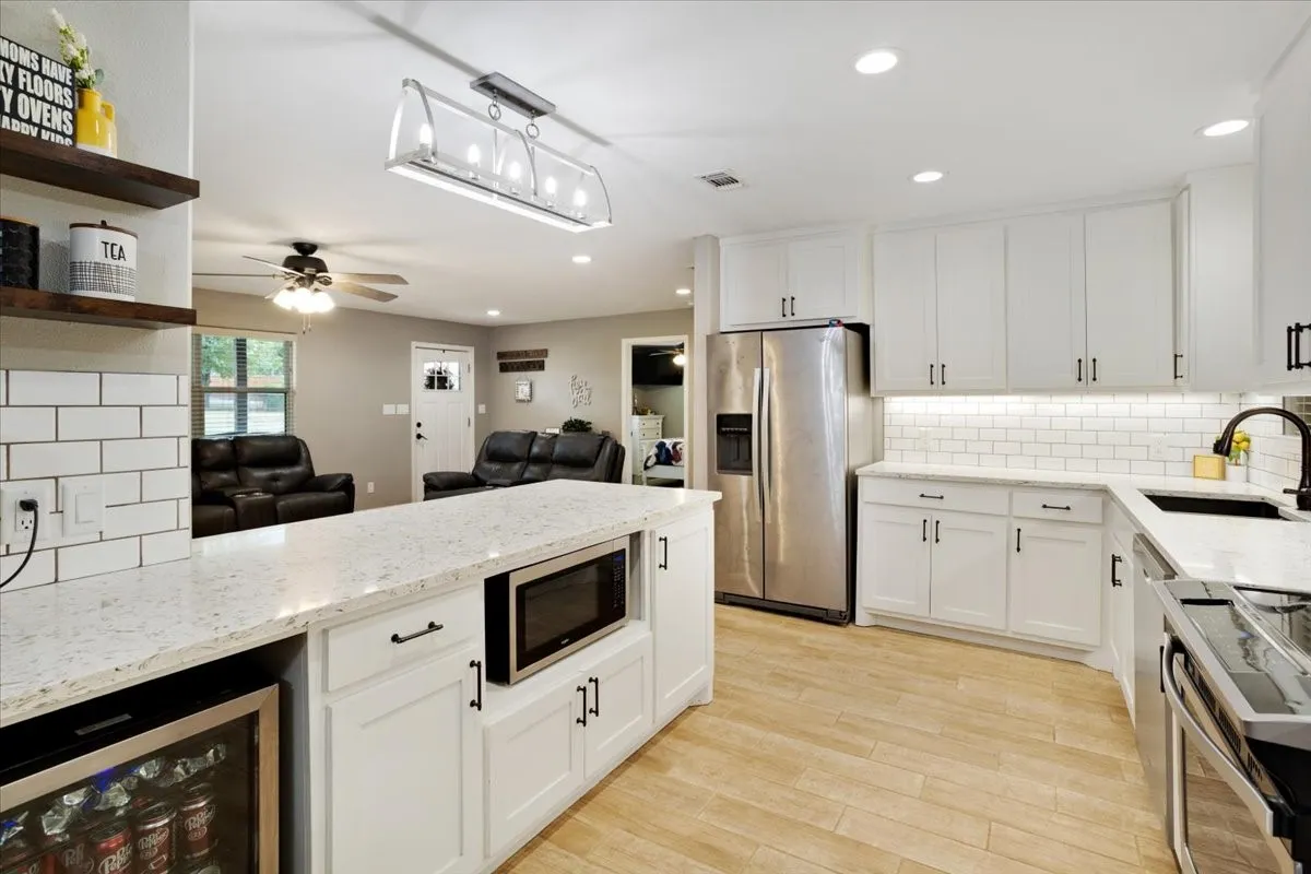 White cabinetry with black hardware, stainless steel appliances, light wood-finish flooring, white subway tile backsplash, and recessed lighting