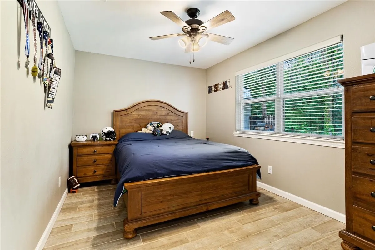 Wood-finish flooring, ceiling fan with integrated lighting, and multiple windows with blinds