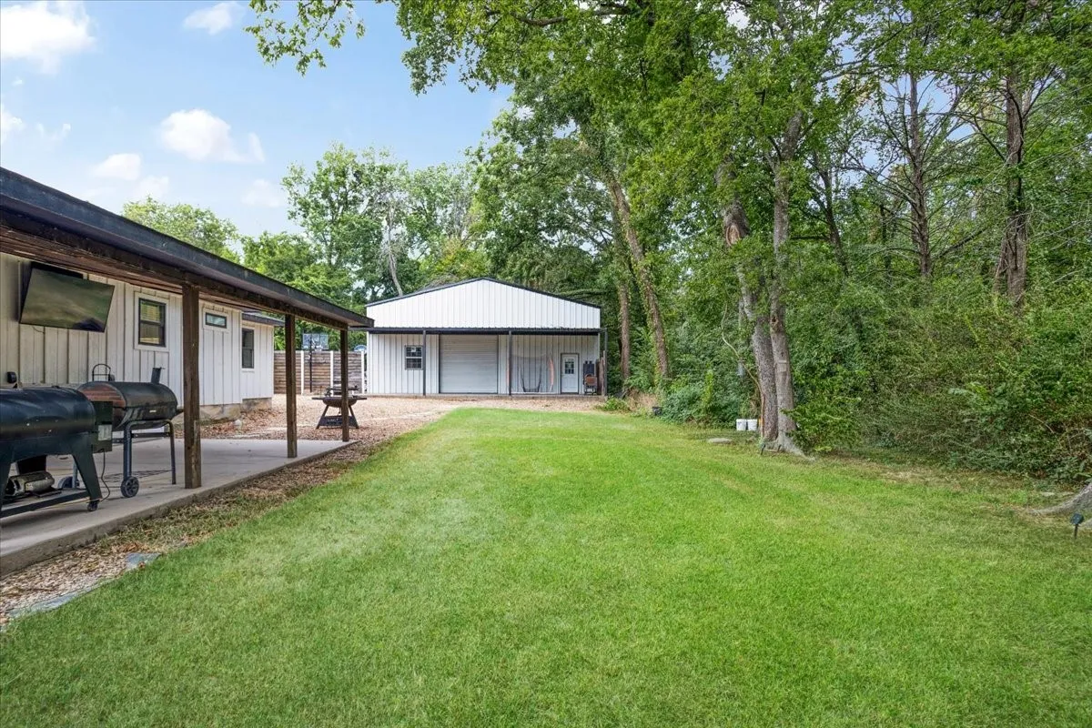 Expansive green lawn with a covered patio, a  40x40 shop with a roll-up door, and mature trees providing natural screening