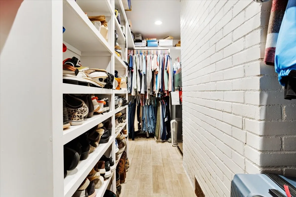 Custom built-in shelving, white brick accent wall, wood-finish flooring, recessed lighting, and garment hanging rods