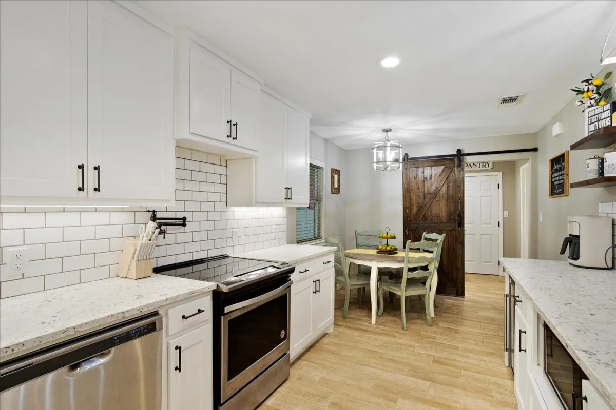 Kitchen featuring white cabinetry, subway tile backsplash, light-colored countertops, wood-finish flooring, and a sliding barn door