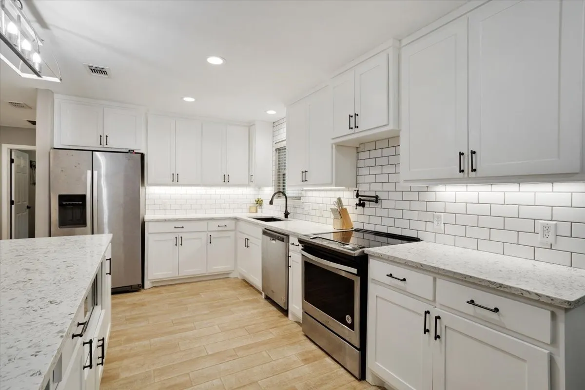 Kitchen featuring white shaker cabinetry, light-toned countertops, subway tile backsplash, stainless steel appliances, and wood-finish flooring