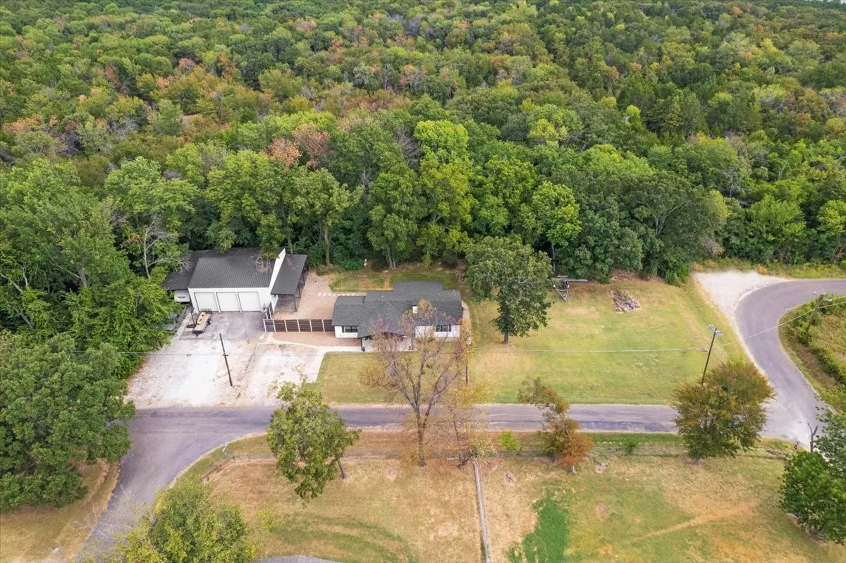 Sprawling property featuring expansive green spaces, multiple structures with a house and a separate garage, and a forested backdrop