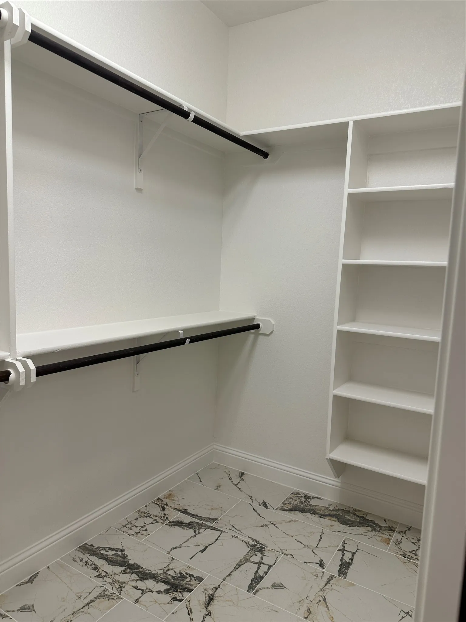 Built-in shelving, two hanging rods, a white painted interior, and marble-look floor tiling